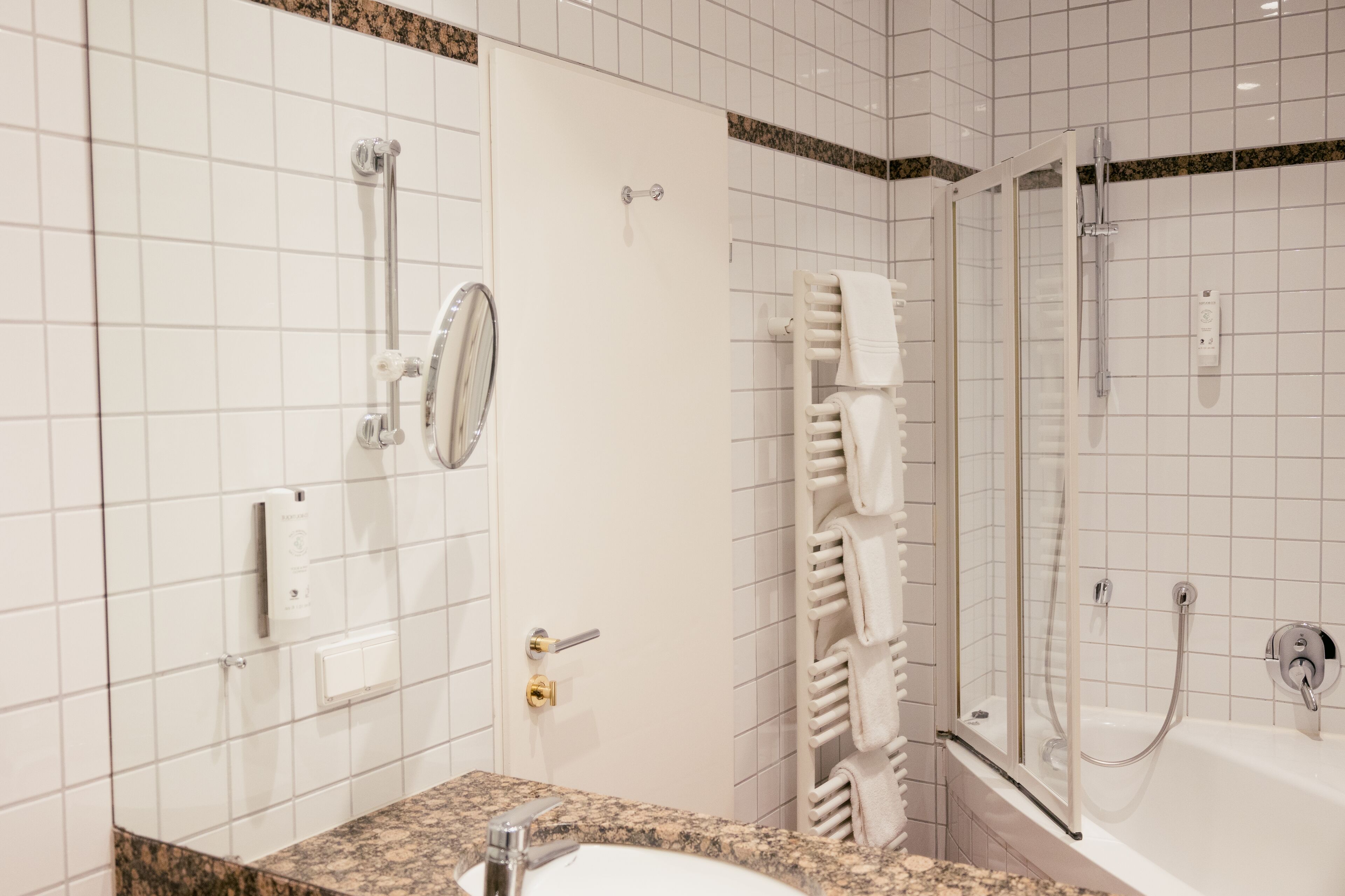 A modern bathroom with a granite countertop, a white sink, a glass shower enclosure, and a towel rack.