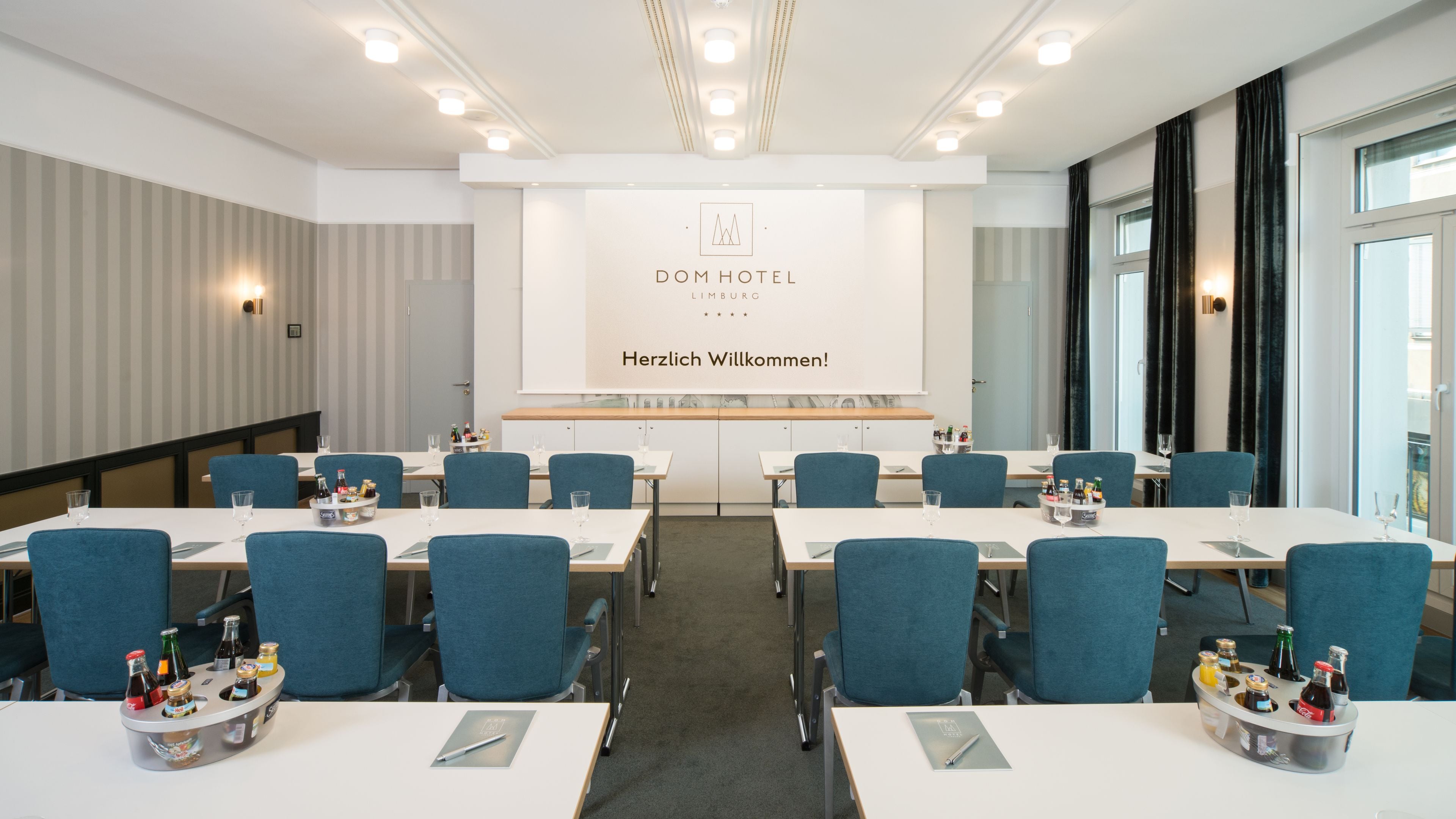 Una sala de conferencias en el Dom Hotel de Limburg, con una pizarra que muestra el nombre del hotel y un mensaje de bienvenida.