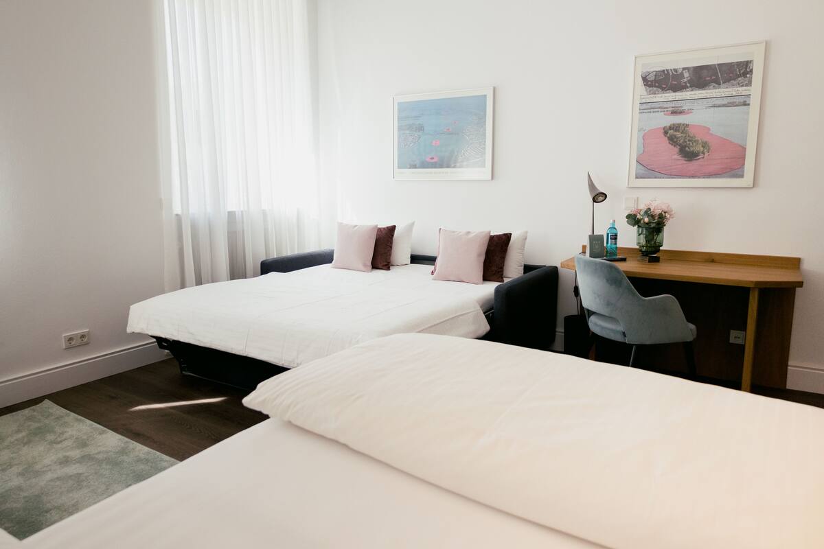 Een hotelkamer met twee bedden, een bureau, een stoel en twee ingelijste foto's aan de muur.