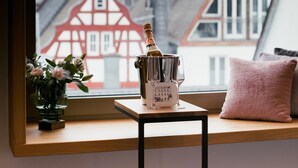 A view from a window with a bottle of champagne, a vase with flowers, and a pink pillow on a wooden ledge. - Dom Hotel Limburg (Limburg an der Lahn)