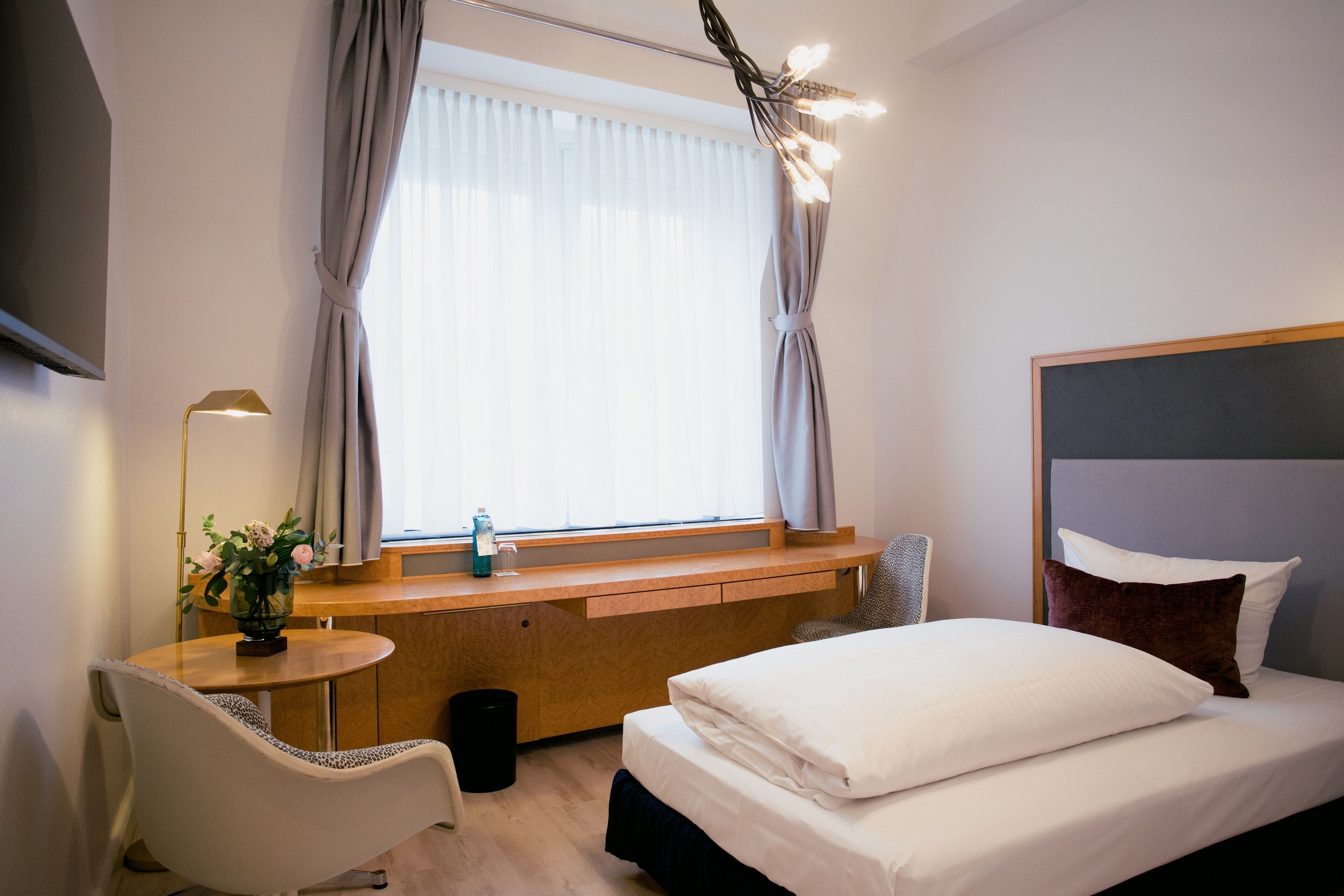 Une chambre d’hôtel moderne équipée d’un lit, d’un bureau, d’une chaise, d’une télévision et d’une fenêtre avec des rideaux.