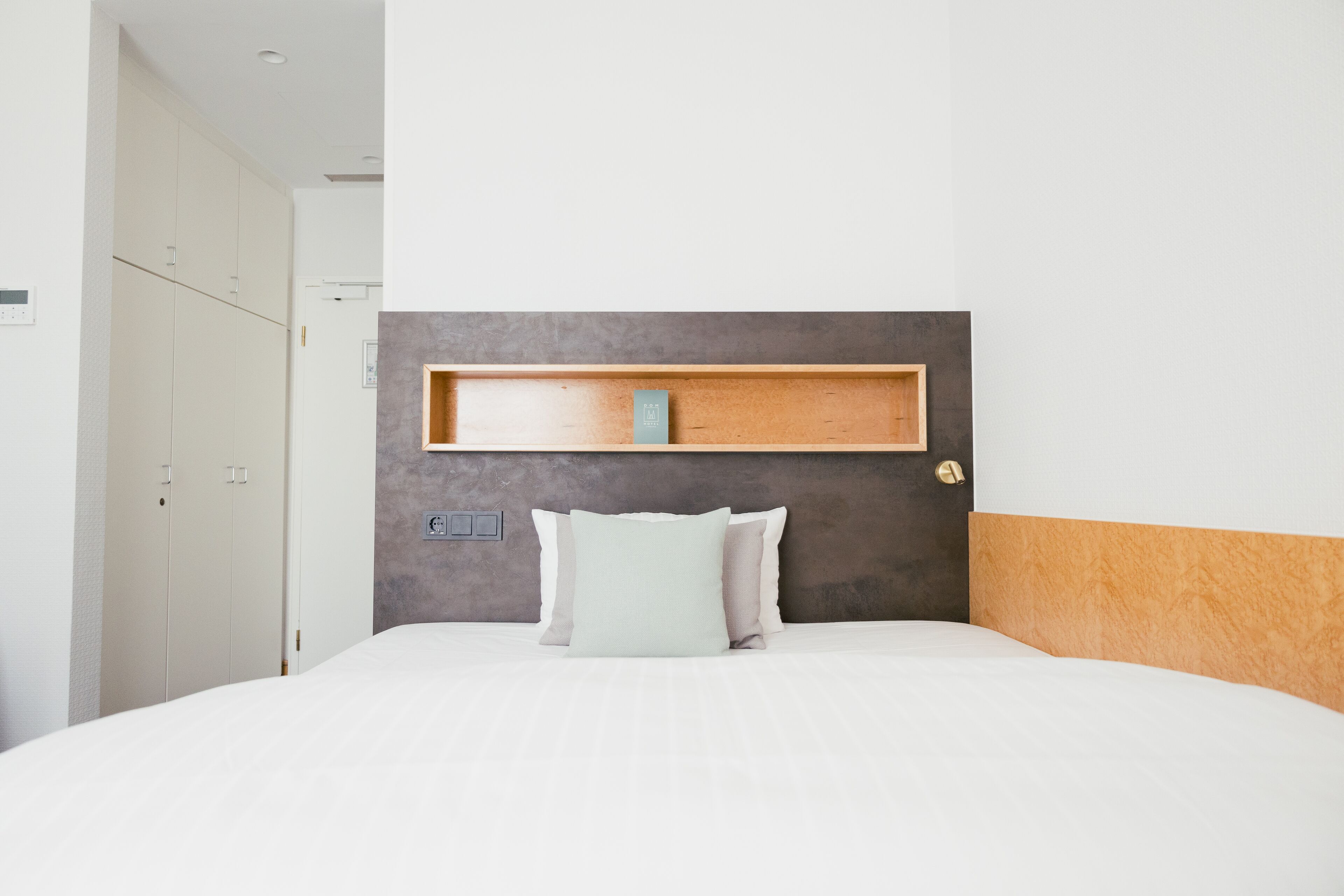 A neatly arranged hotel room with a bed, a bedside table, and a wardrobe.