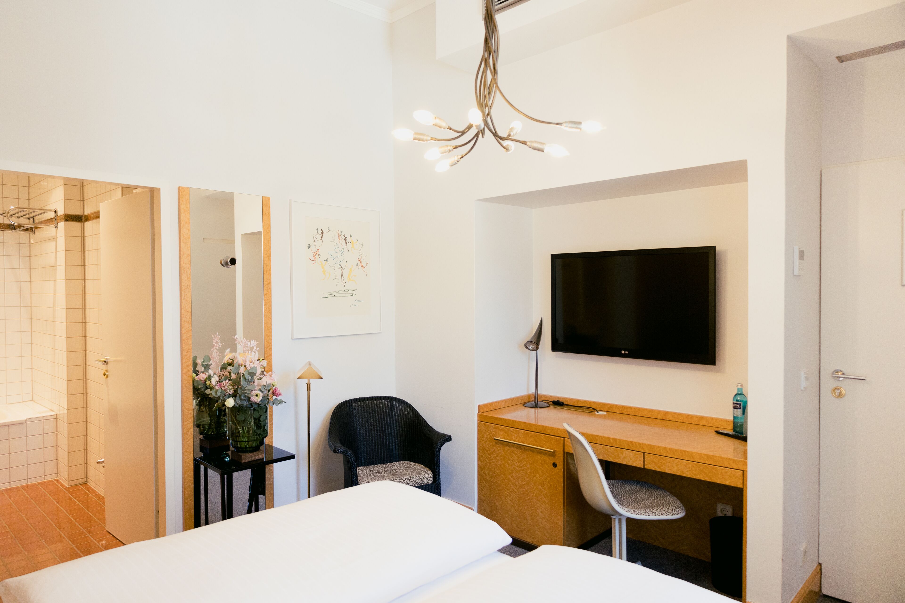 A hotel room with a bed, a desk, a chair, a TV, a shower, and a mirror.
