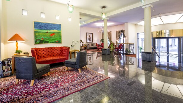 A spacious lobby with a red sofa, a patterned rug, and a large painting on the wall. - Dom Hotel Limburg (Limburg an der Lahn)