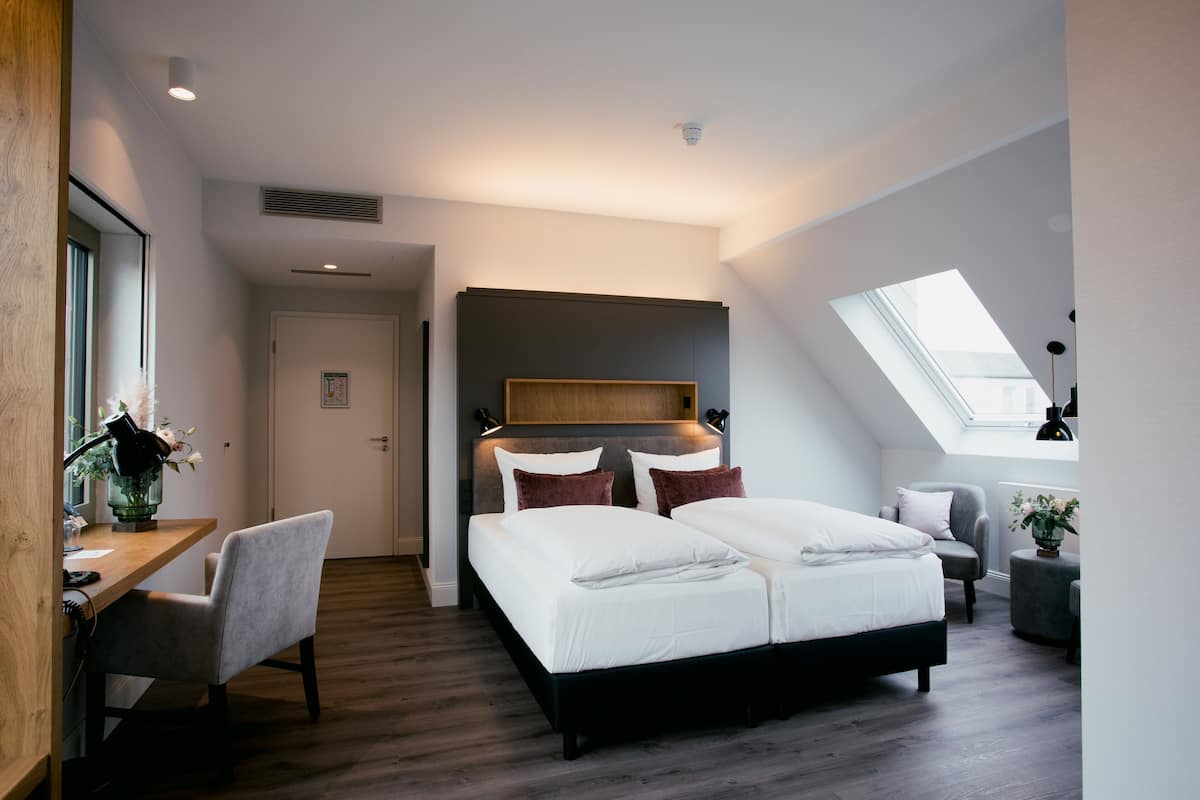 Een moderne slaapkamer met een groot bed, een bureau en een stoel. Boven het bed is een dakraam.
