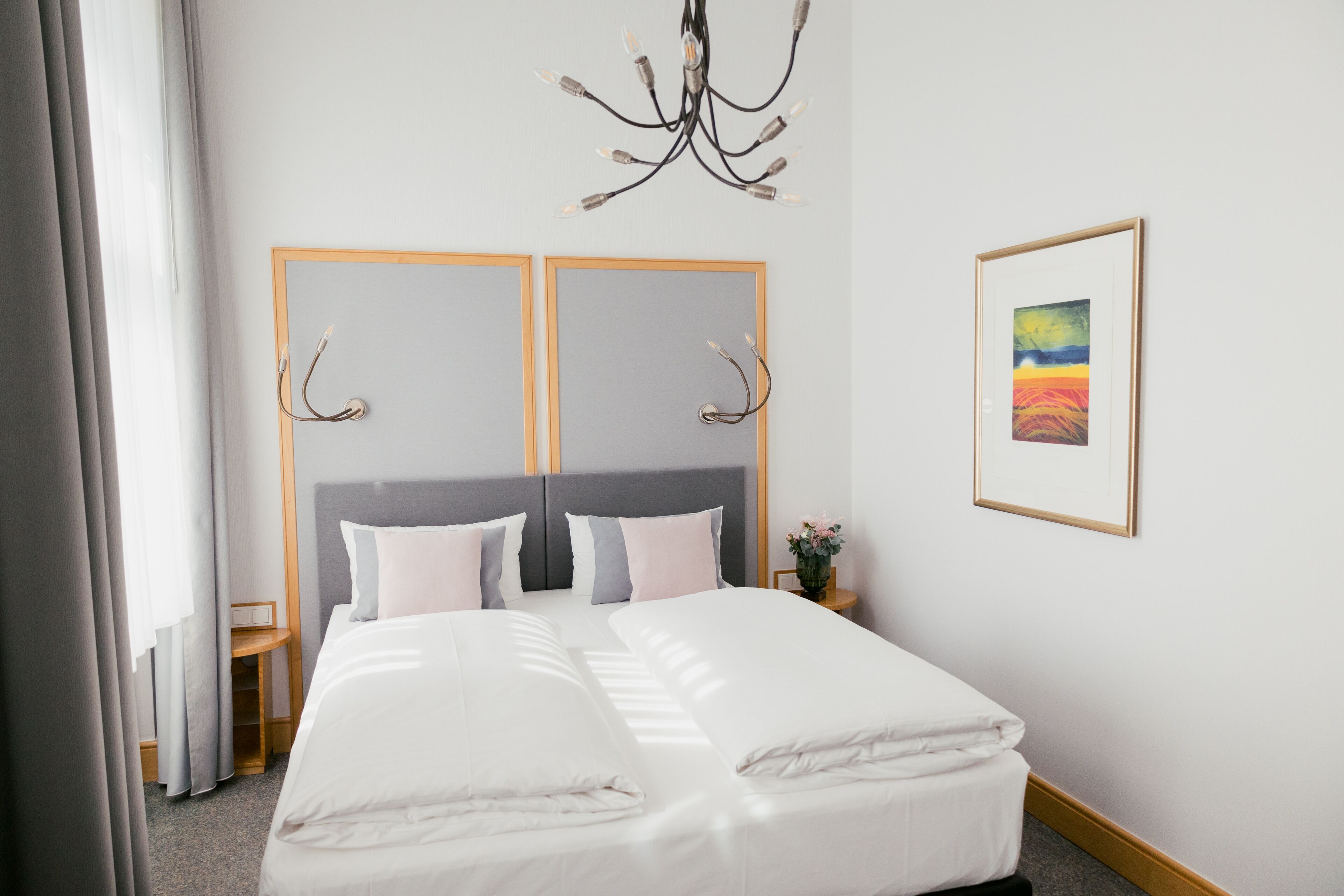 Een hotelkamer met een groot bed, twee nachtkastjes, een kroonluchter en een ingelijst schilderij aan de muur.