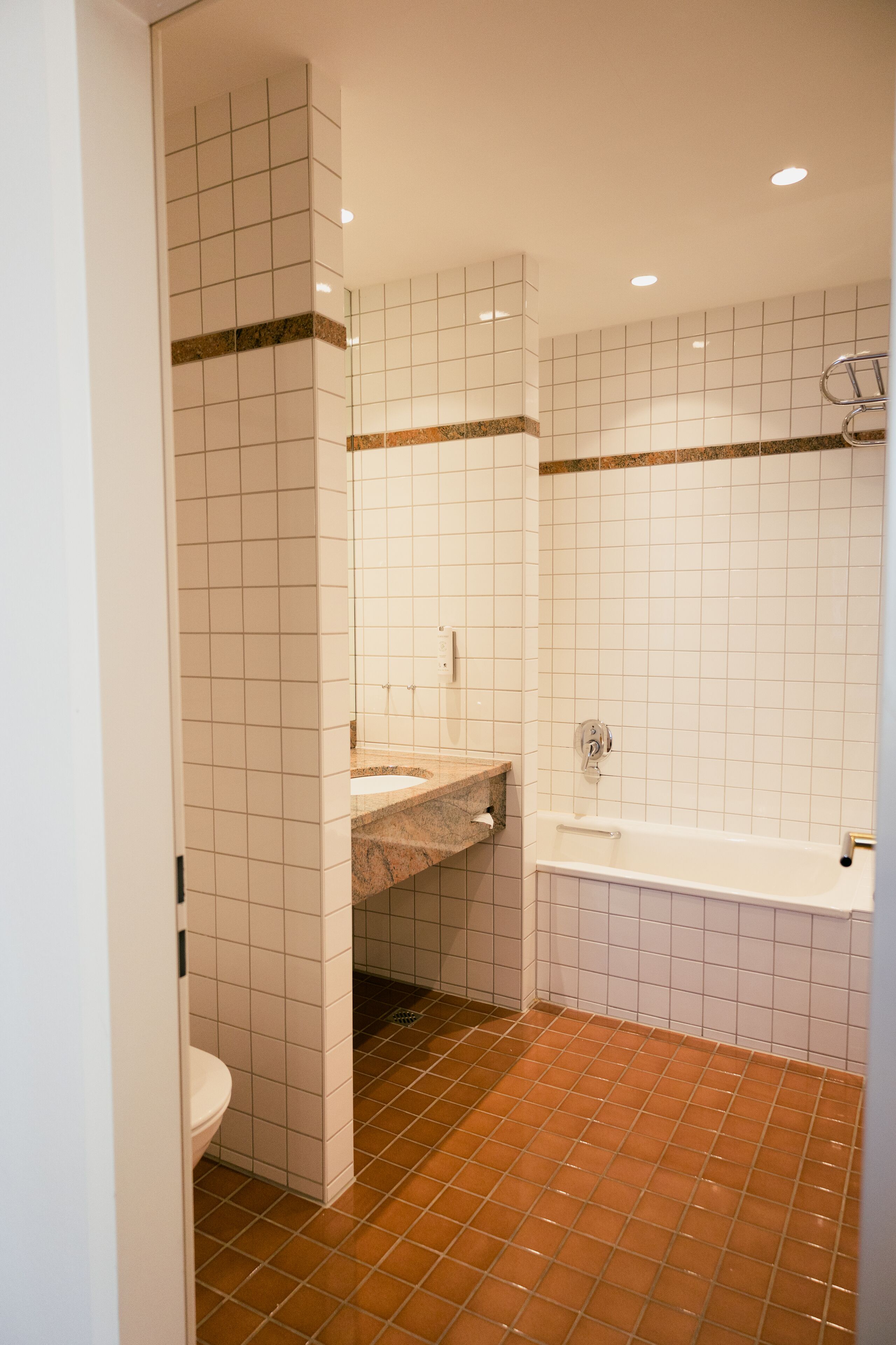 A bathroom with white tiled walls, a brown tiled floor, a sink, and a bathtub.