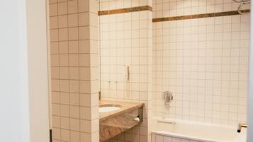 A bathroom with white tiled walls, a brown tiled floor, a sink, and a bathtub.