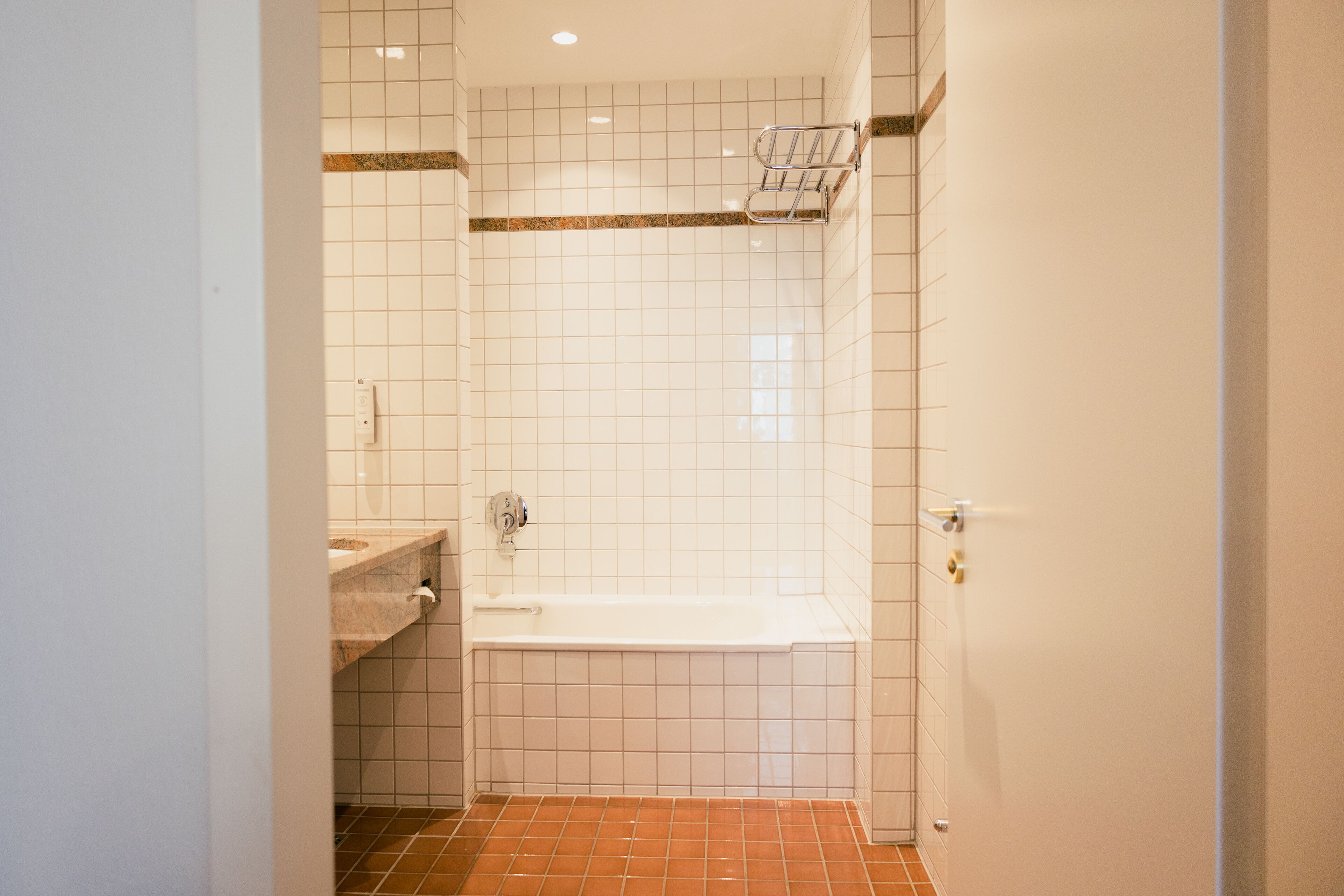 A bathroom with white tiled walls, a bathtub, and a tiled floor.