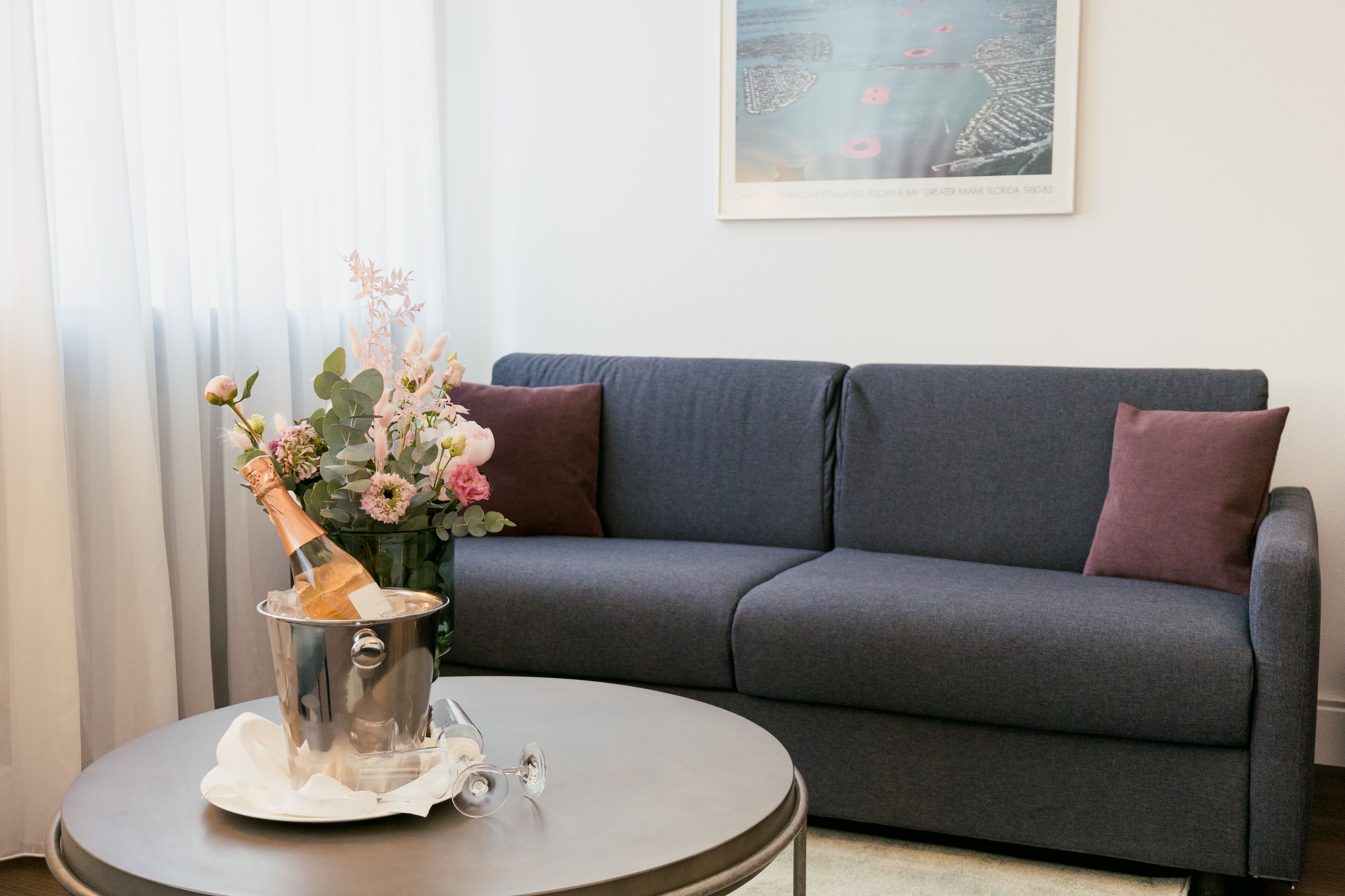 A modern living room with a grey sofa, a round coffee table, and a champagne bottle in a bucket.