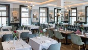 A restaurant with multiple tables set for dining, featuring a bar area with cushioned seating. - Dom Hotel Limburg (Limburg an der Lahn)