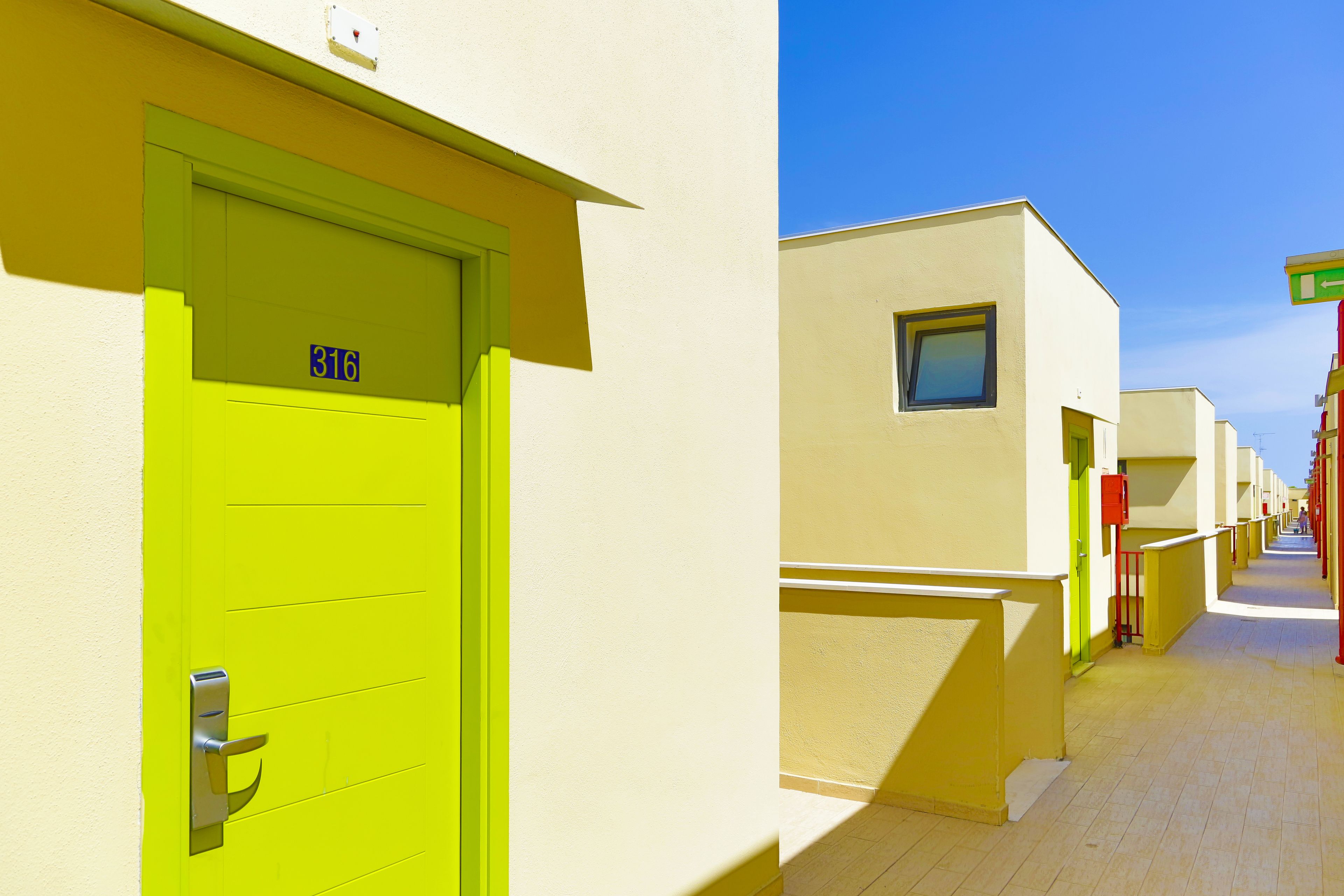 A row of hotel rooms with a bright green door, numbered 316, and a clear sky.