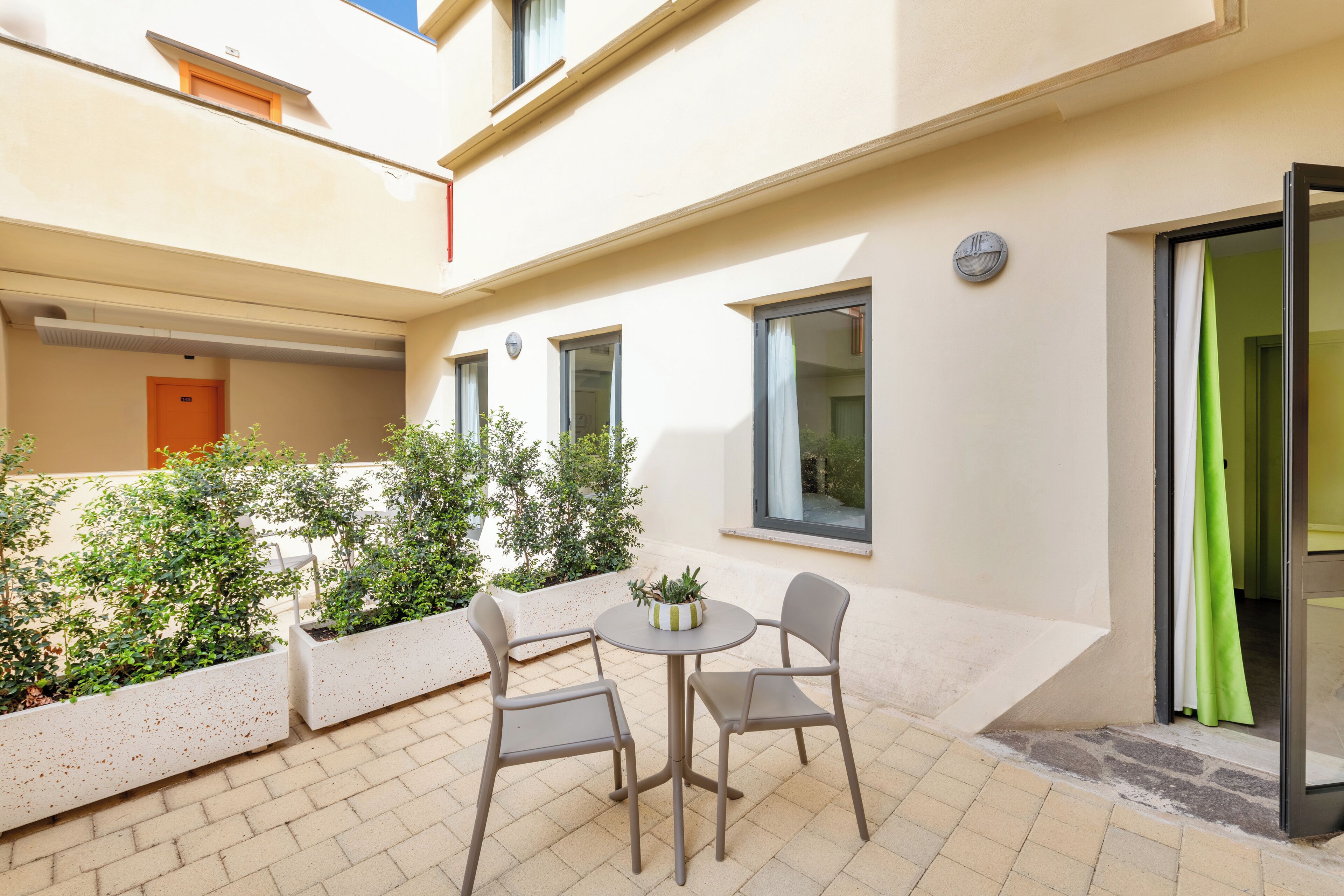 A courtyard with a table and chairs, surrounded by planters and a door.