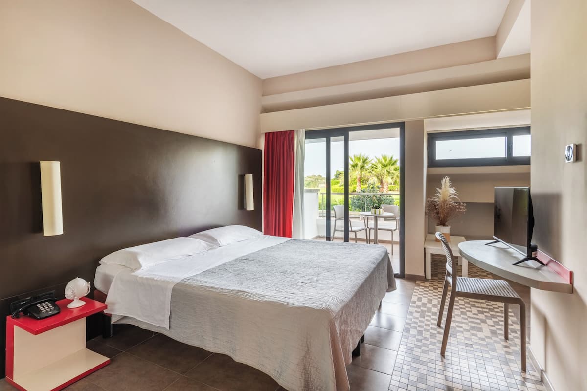 A hotel room with a bed, a desk with a telephone, a TV, and a view of the outdoors.