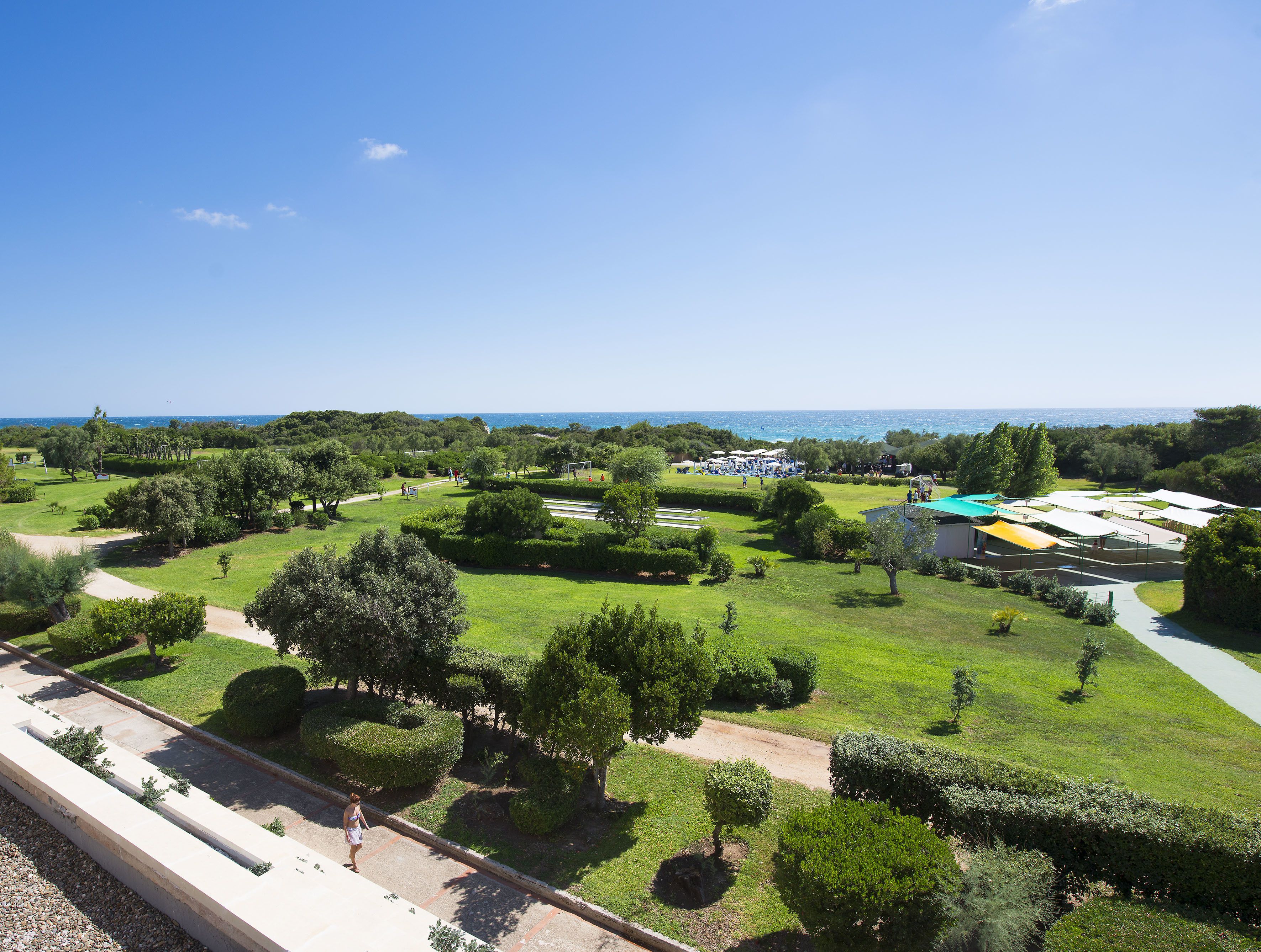 A golf course with a clear view of the sea, surrounded by lush greenery and a few buildings.