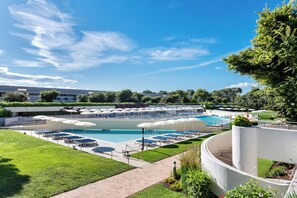 A pool area with lounge chairs and umbrellas, surrounded by greenery and a clear sky. - VOI Alimini Resort (Otranto)