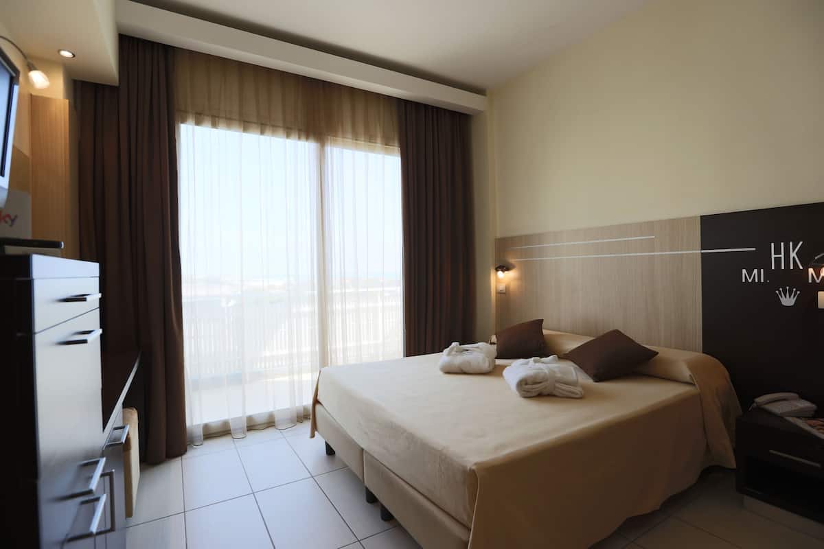 Ein Hotelzimmer mit Bett, Schreibtisch, Stuhl, Fernseher und einem Fenster mit Vorhängen.