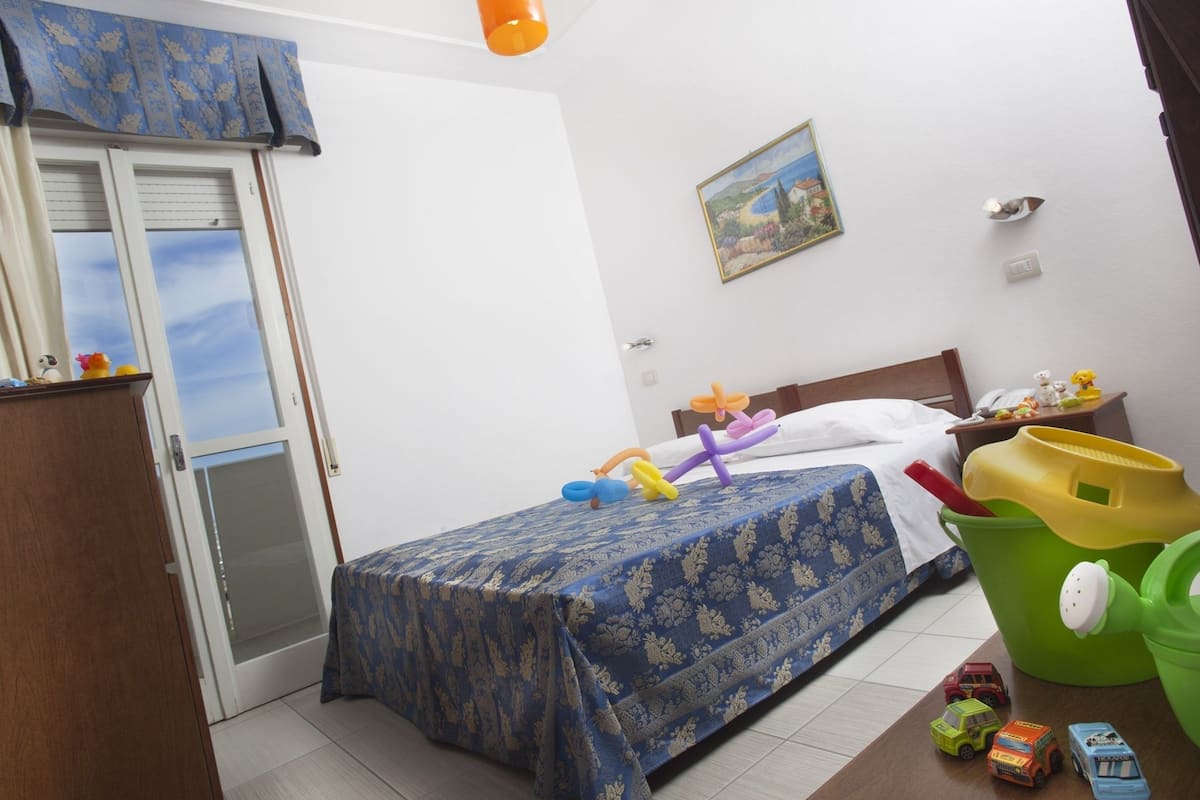 Ein Schlafzimmer mit einem Bett, einem Nachttisch, einem grünen Eimer und Spielzeugautos auf dem Boden.