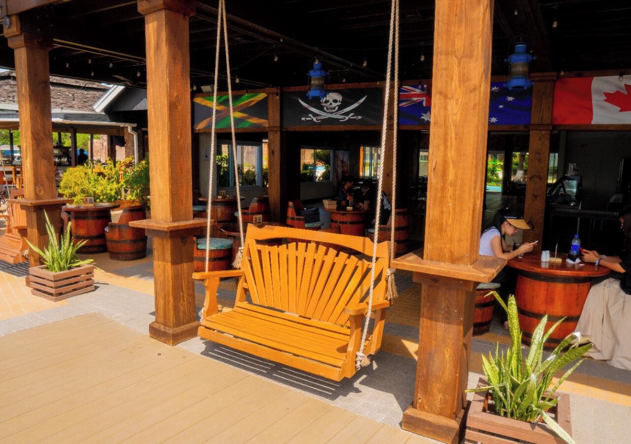 A wooden swing chair suspended by ropes, surrounded by wooden pillars and potted plants.