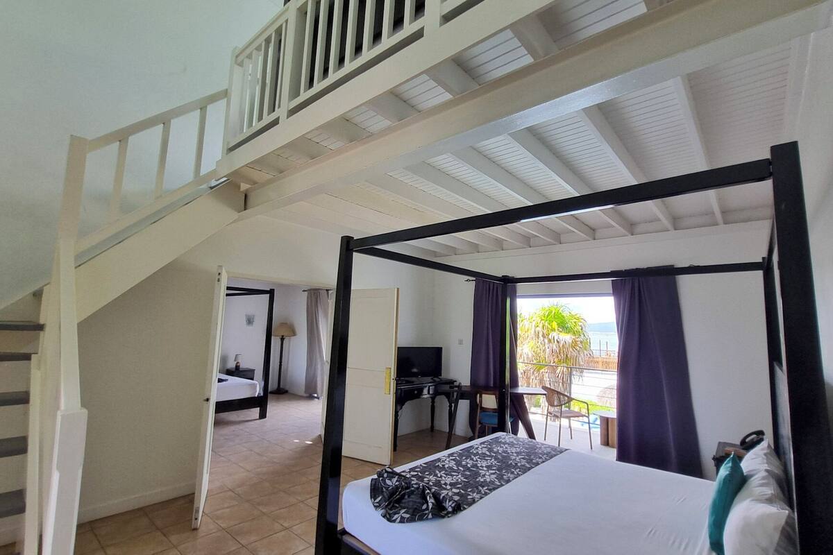 Une chambre à coucher avec un lit à baldaquin, un escalier, un bureau avec une chaise et une vue sur l’extérieur.