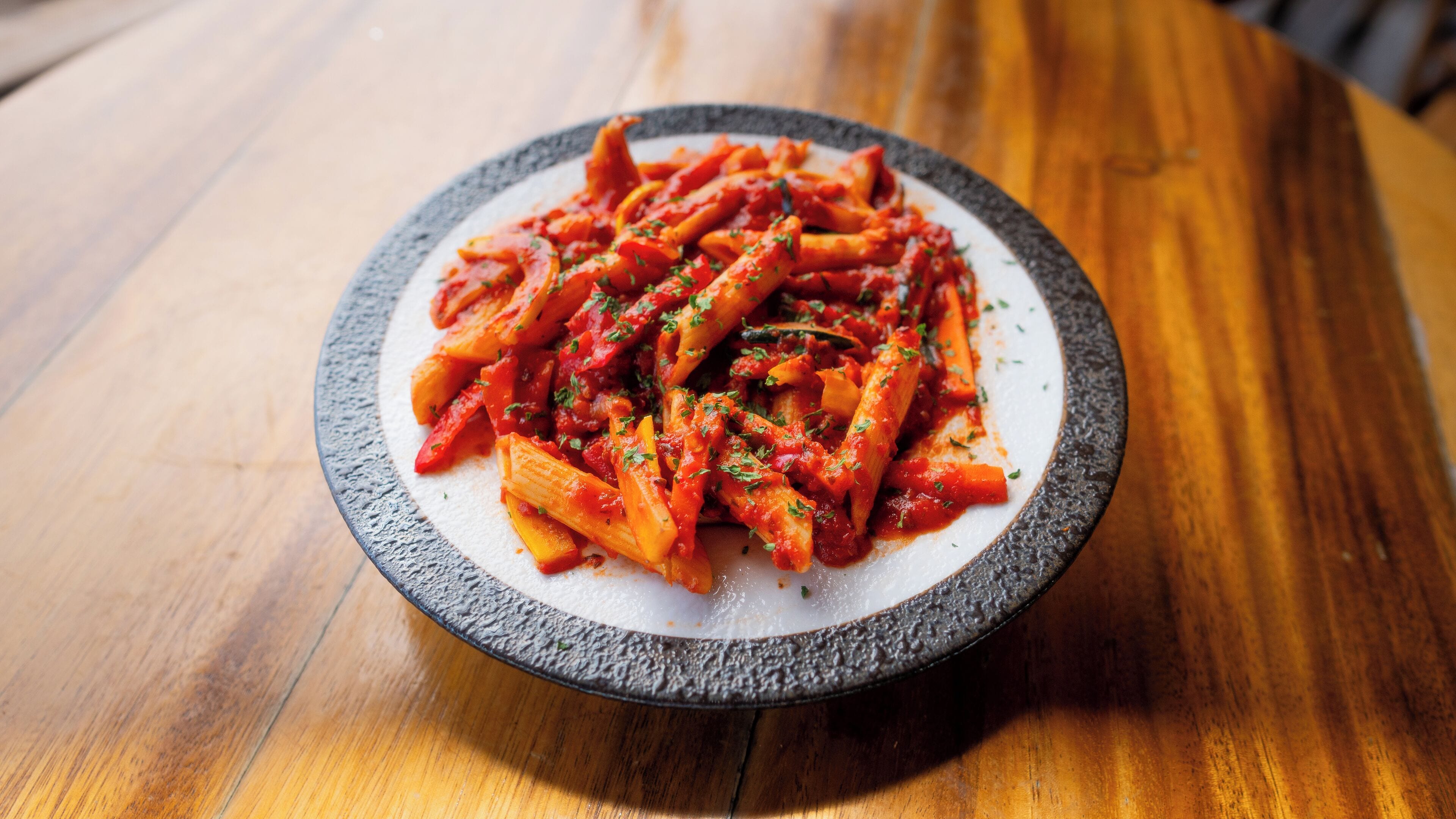 A plate of pasta with a tomato-based sauce, garnished with herbs, on a round ceramic plate.