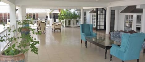 A spacious indoor area with a glass table and blue chairs, surrounded by white railings and potted plants.