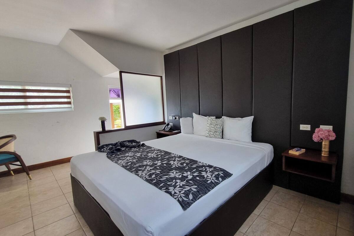 Une chambre d’hôtel moderne avec un grand lit, un bureau et une tête de lit sombre.