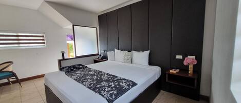 A modern hotel room with a large bed, a desk, and a dark headboard.