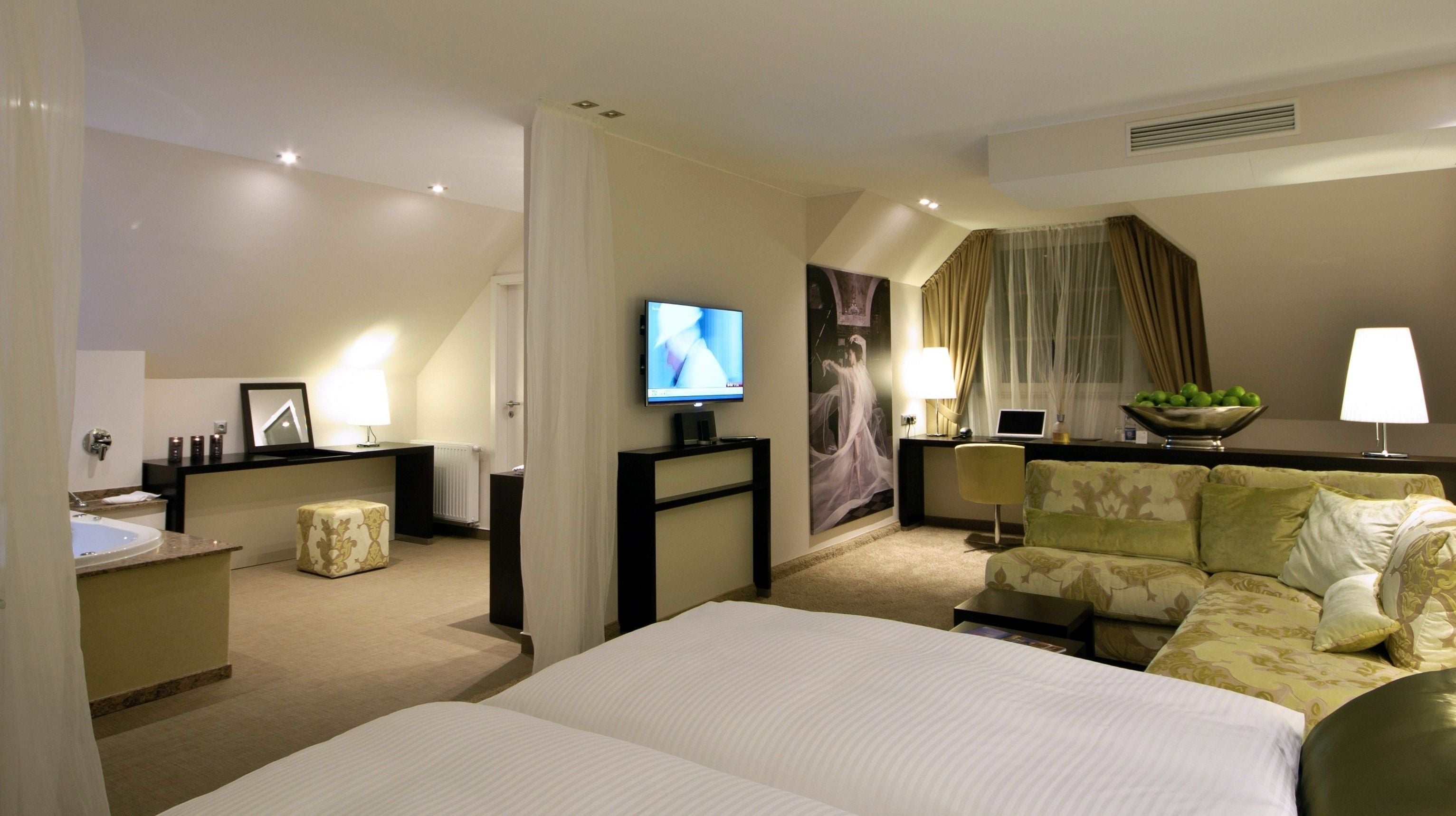 A hotel room with a large bed, a desk with a computer, a television, and a seating area with a couch.