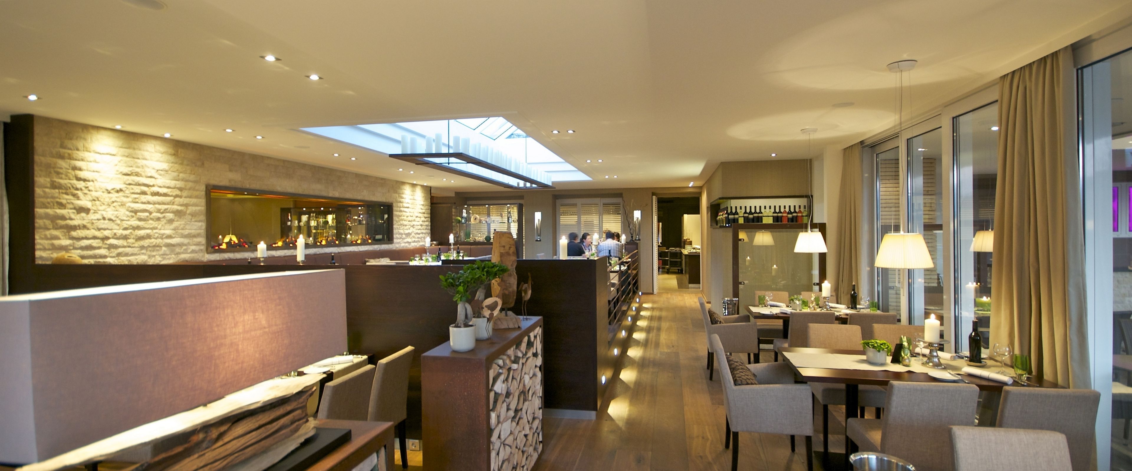 Un hall d’hôtel moderne doté d’un bar, de différents espaces aménagés pour s’asseoir et d’une verrière.