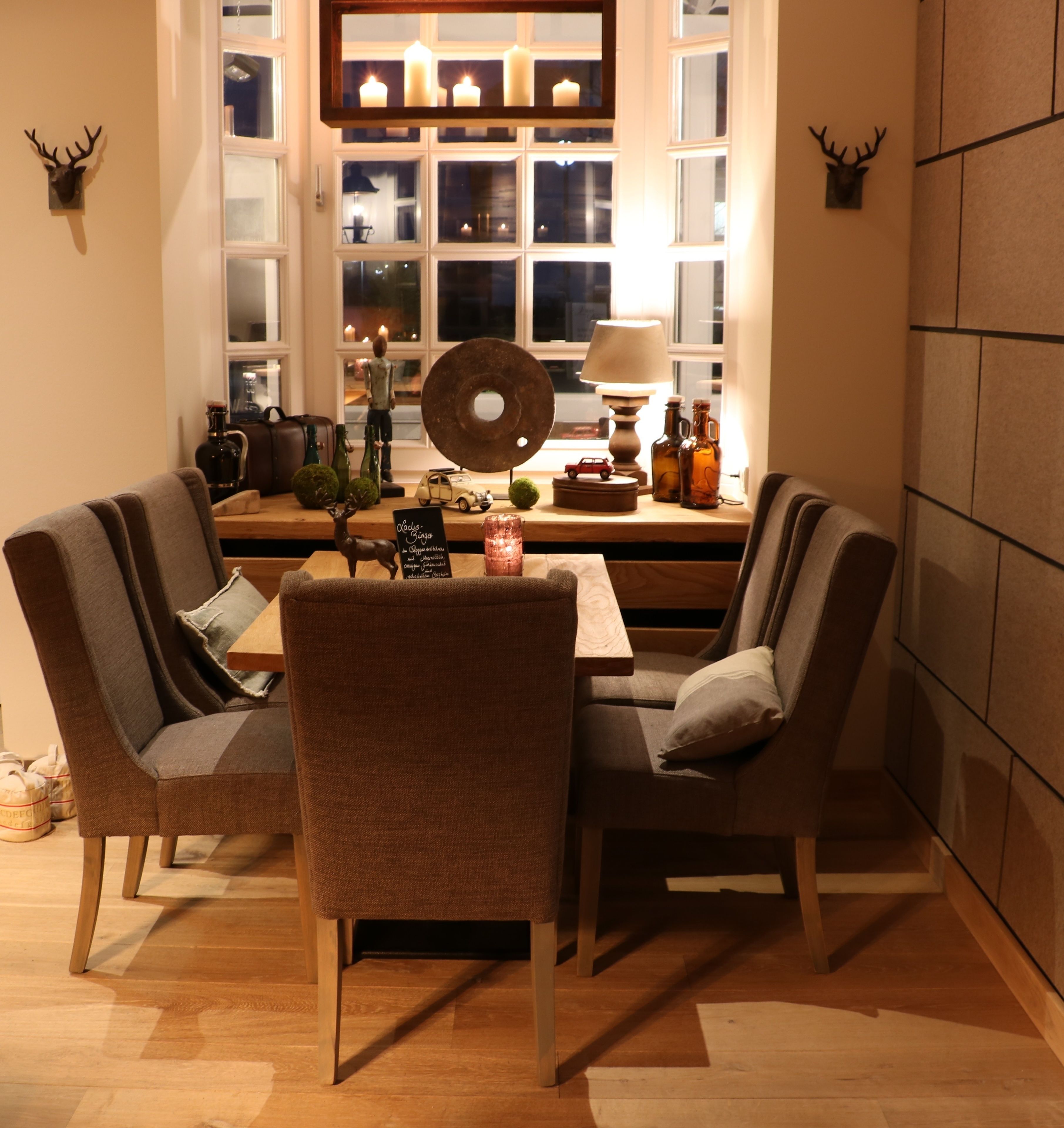 A dining area with a table set for four, surrounded by upholstered chairs. A large window with multiple panes is behind the table, displaying a view of the night sky.