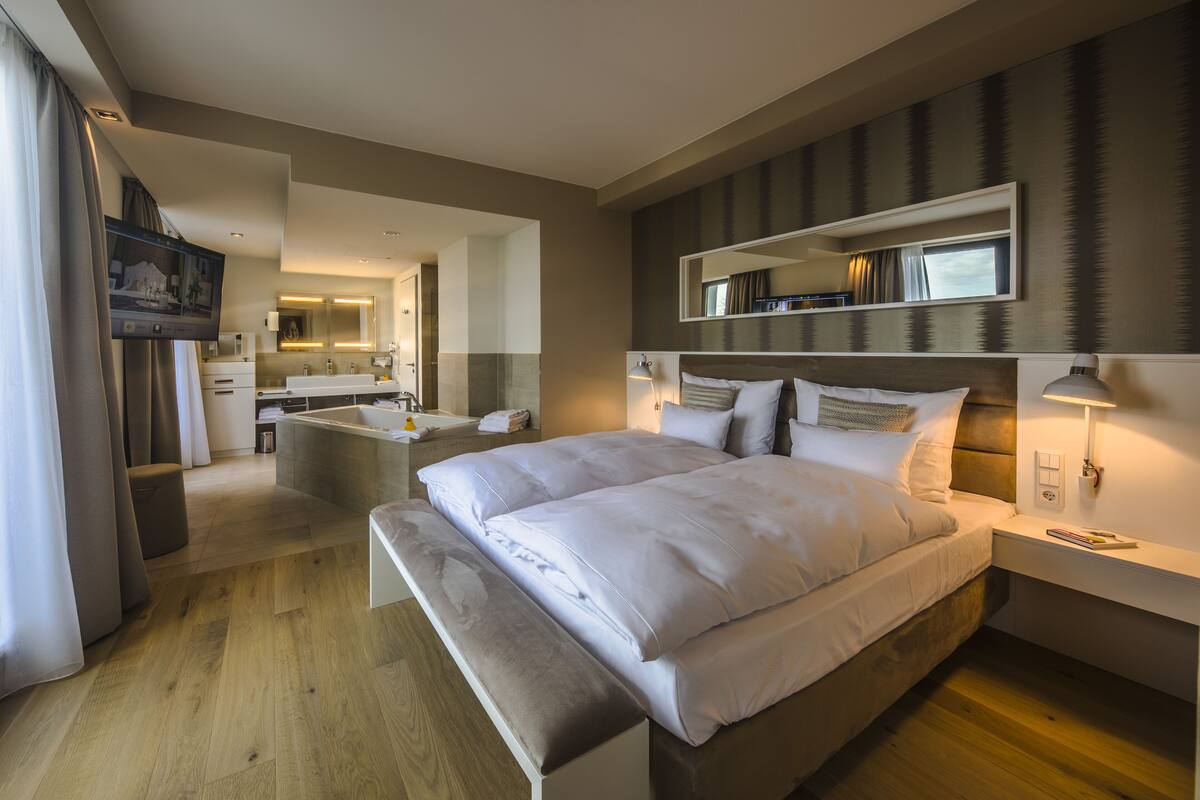 Een moderne hotelkamer met een groot bed, nachtkastje, badkamer met wastafel en spiegel, en een televisie.
