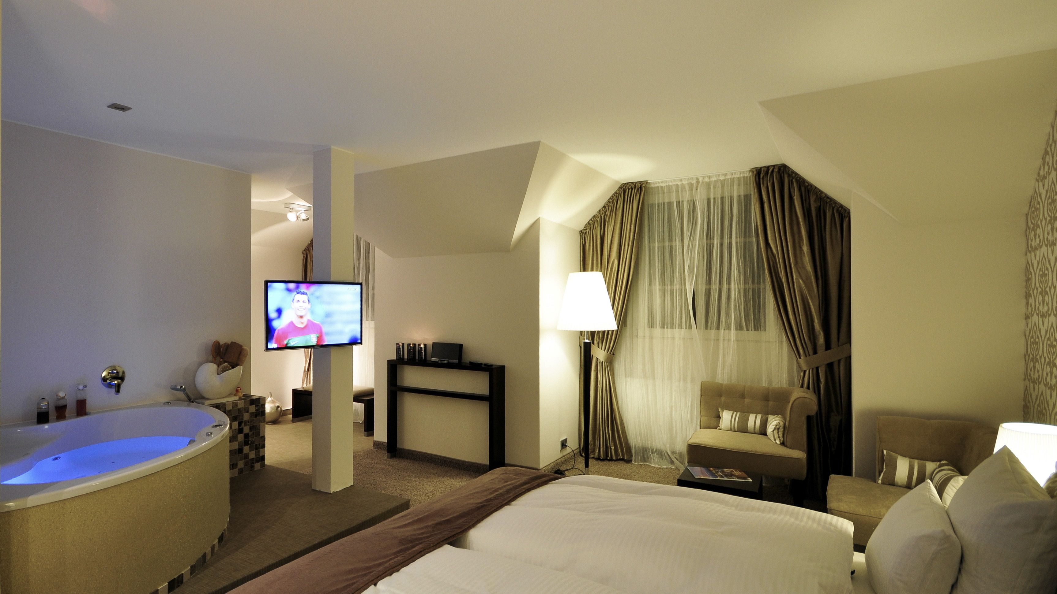 A hotel room with a large bed, a bathtub, a television, a desk, and a chair.