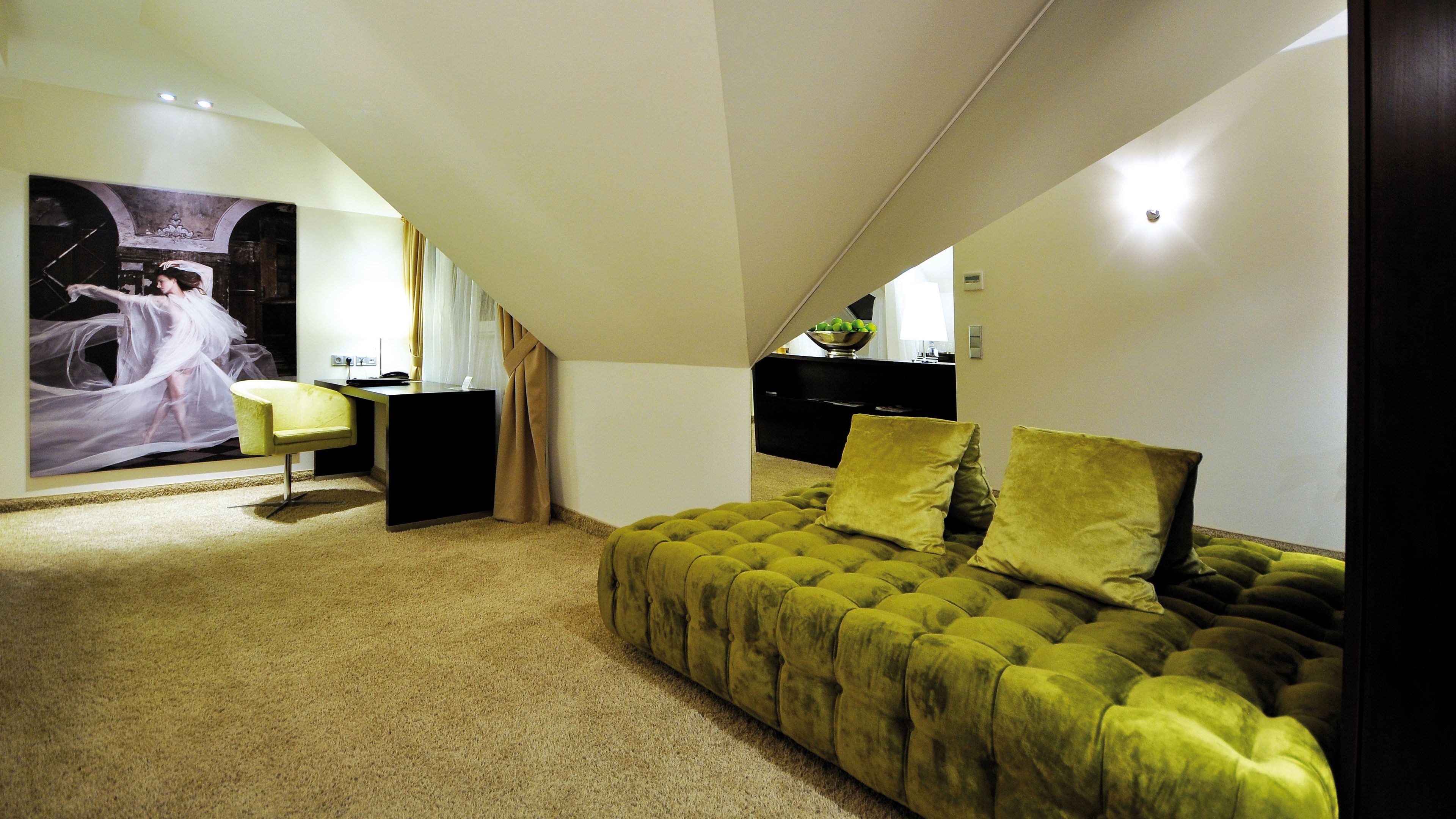 A modern bedroom with a tufted green sofa, a desk, and a large painting on the wall.
