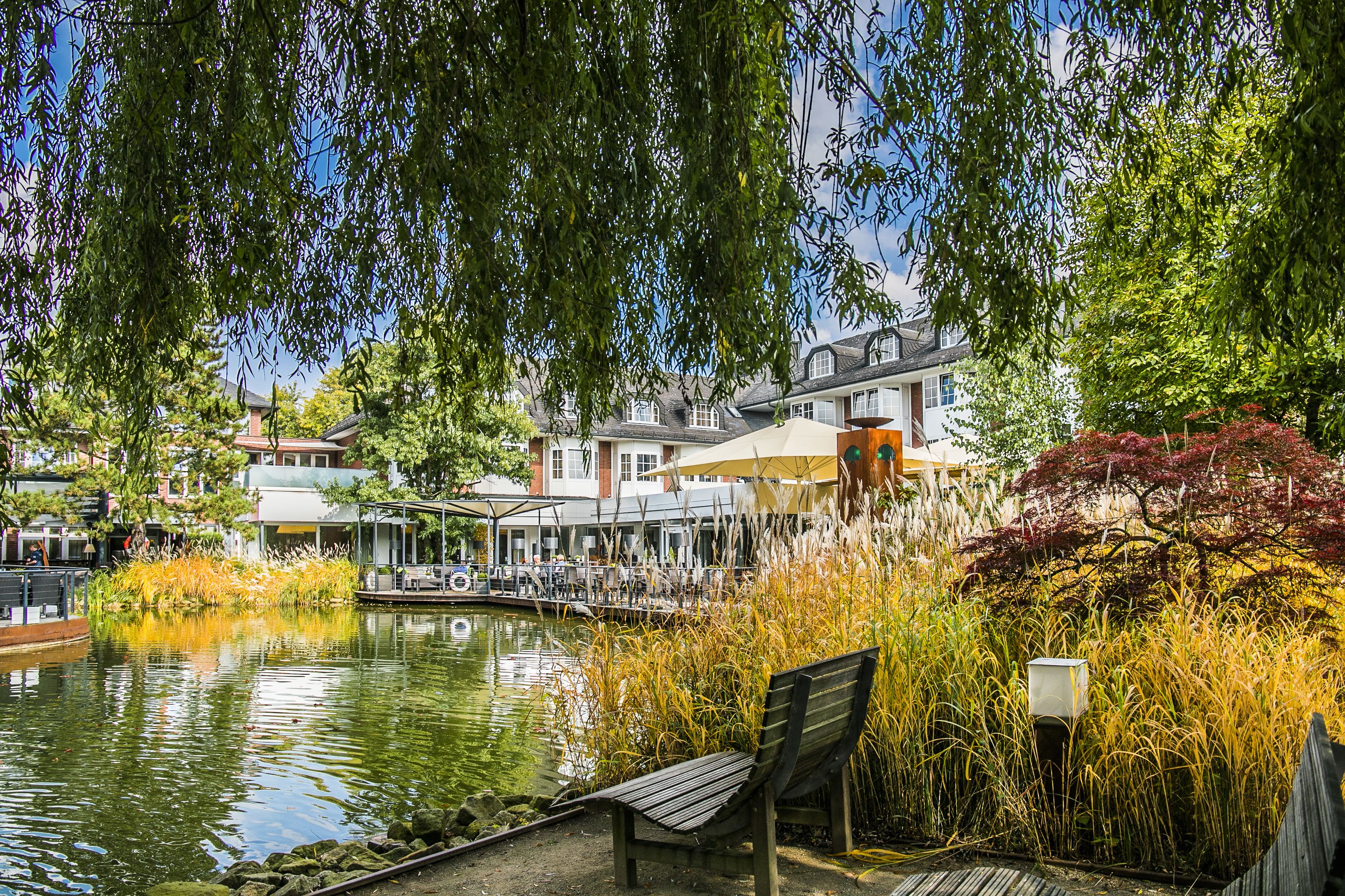 Ein Uferweg mit Bank, einem kleinen Boot und einem Restaurant mit Terrassensitzplatz.