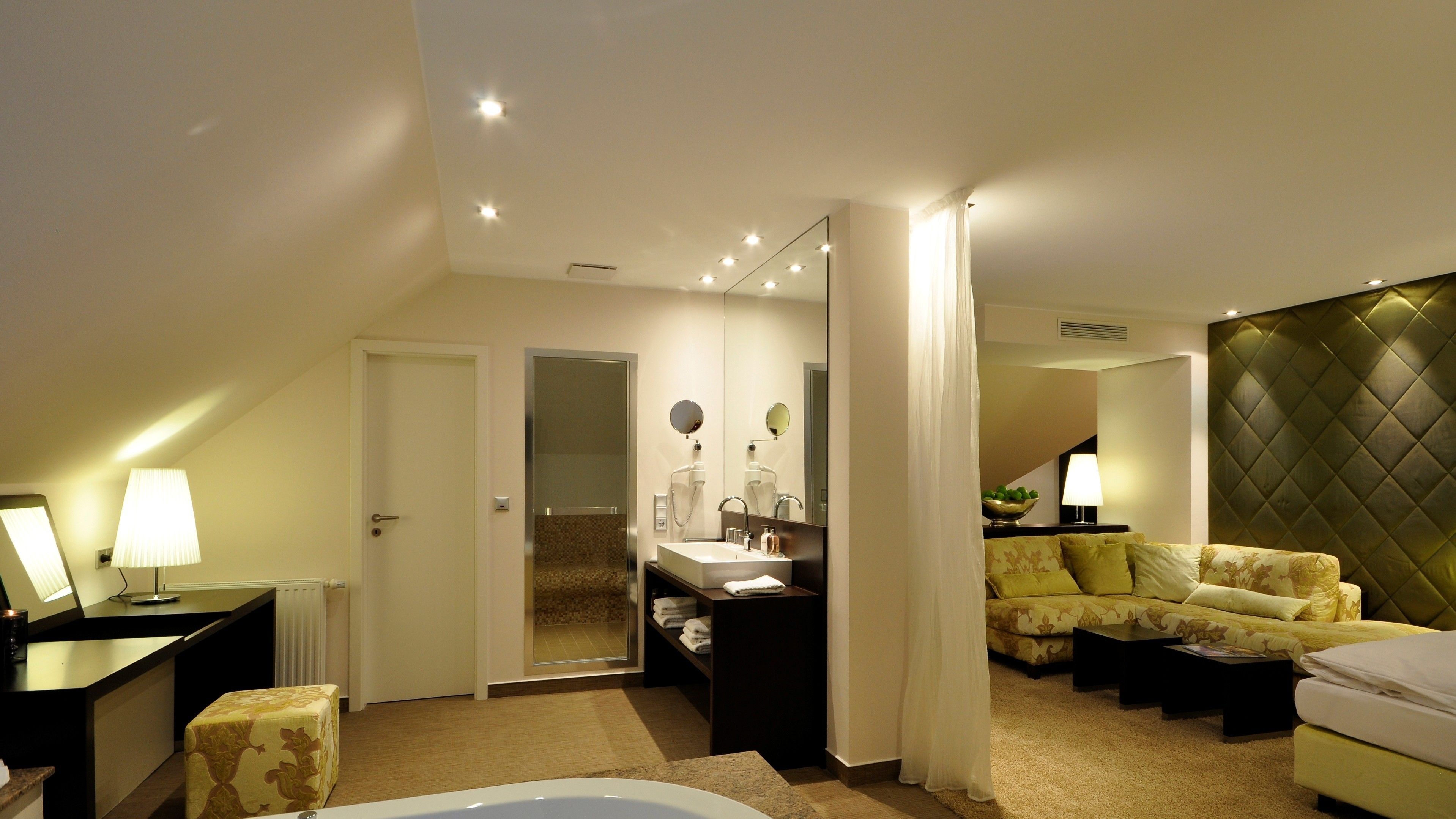 Una habitación de hotel moderna con una cama grande, una zona de estar con sofá, un baño independiente con bañera y un comedor con mesa y sillas.