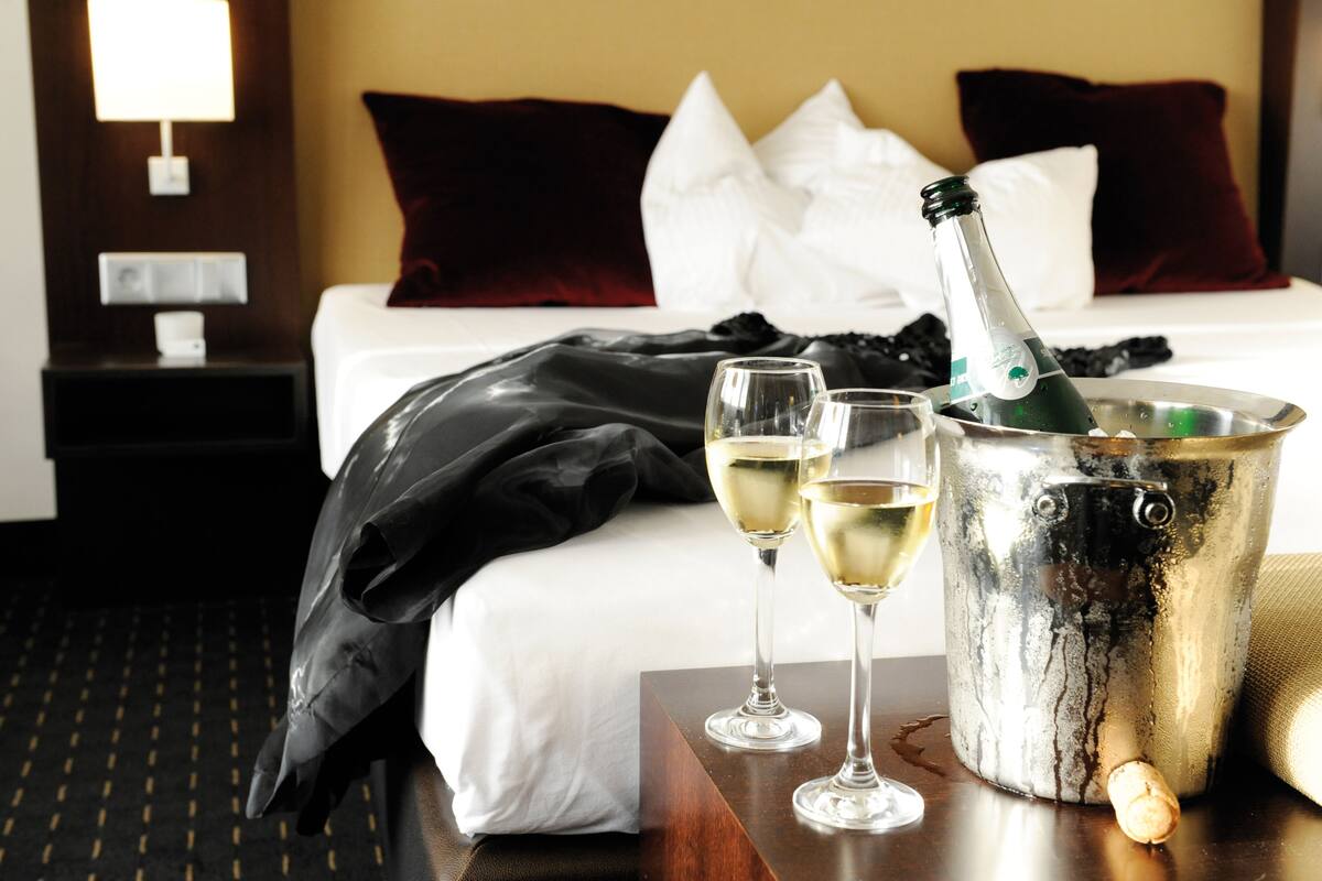 Een hotelkamer met een bed, een nachtkastje, een fles champagne en twee champagneglazen.