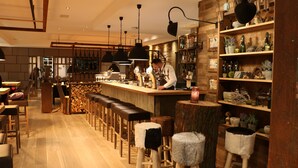 Angolo bar con sgabelli di legno, un barista ed scaffali con bottiglie e decorazioni.