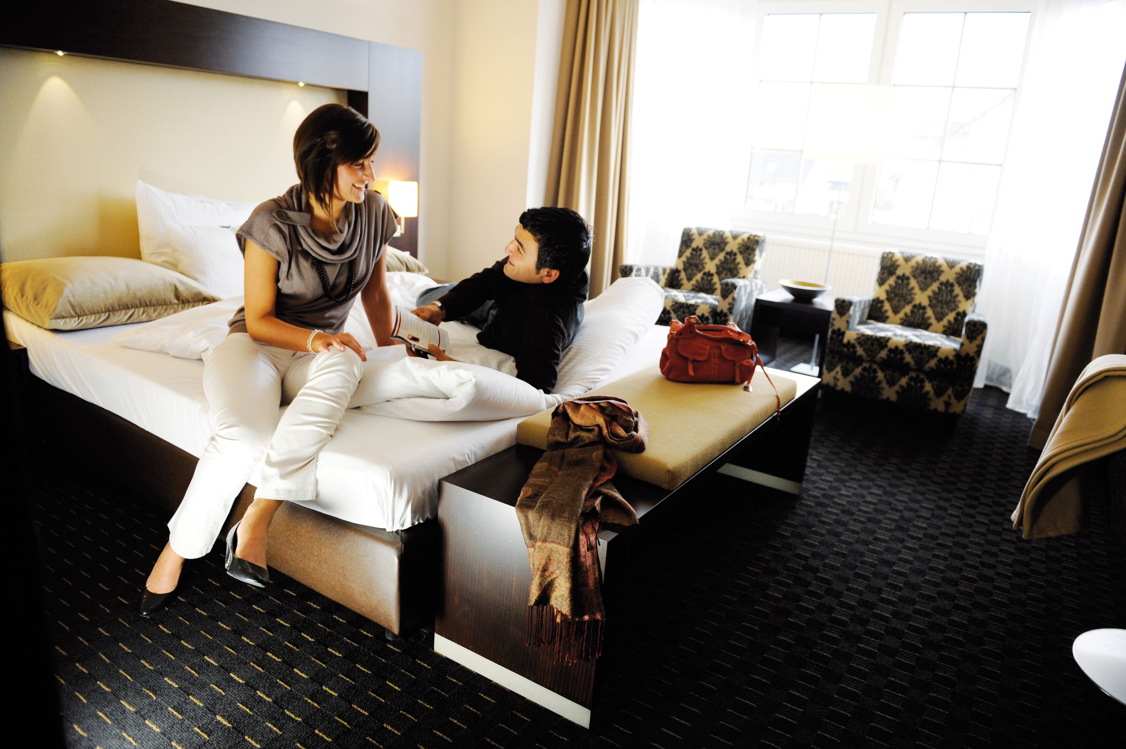 Een hotelkamer met een bed, nachtkastje, stoel en raam.