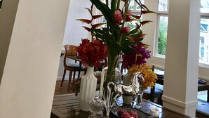 A well-lit room with hanging lantern-style lights, a large potted plant, and a table with various decorative items including flowers and a silver horse sculpture. - Bon Ca Va (Chiang Mai)