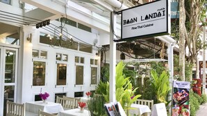 An outdoor seating area with tables and chairs, a sign for Boan Landai Fine Thai Cuisine, and lush greenery. - Bon Ca Va (Chiang Mai)