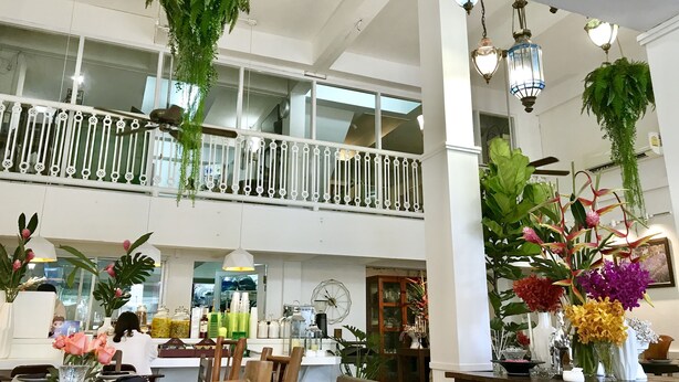 A spacious indoor area with a high ceiling, a balcony with white railings, and various plants and flowers arranged on tables. - Bon Ca Va (Chiang Mai)