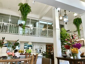 A spacious indoor area with a high ceiling, a balcony with white railings, and various plants and flowers arranged on tables. - Bon Ca Va (Chiang Mai)