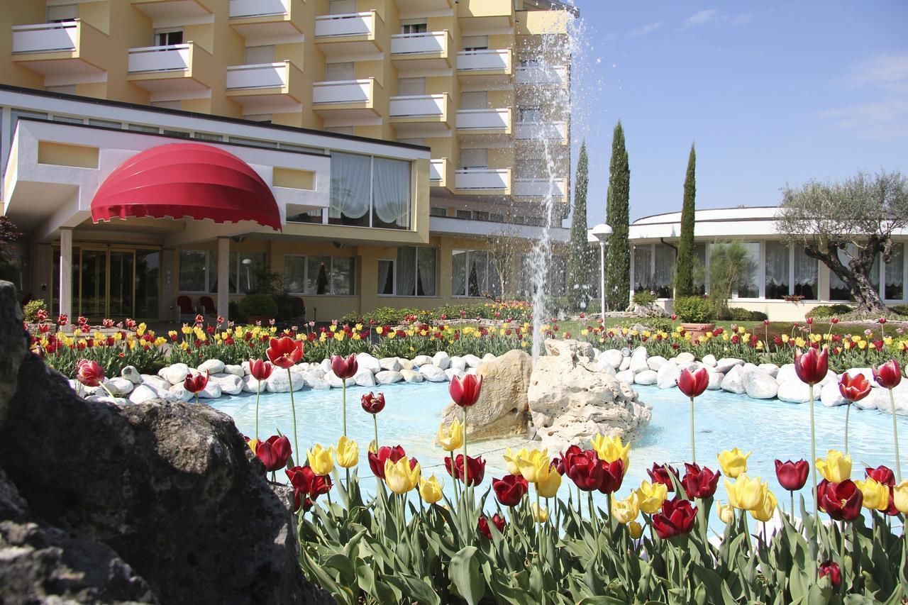 Un hotel con piscina rodeado de tulipanes de colores, una fuente y un paraguas rojo.