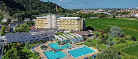 A hotel with multiple swimming pools, a large garden, and a view of the surrounding landscape.