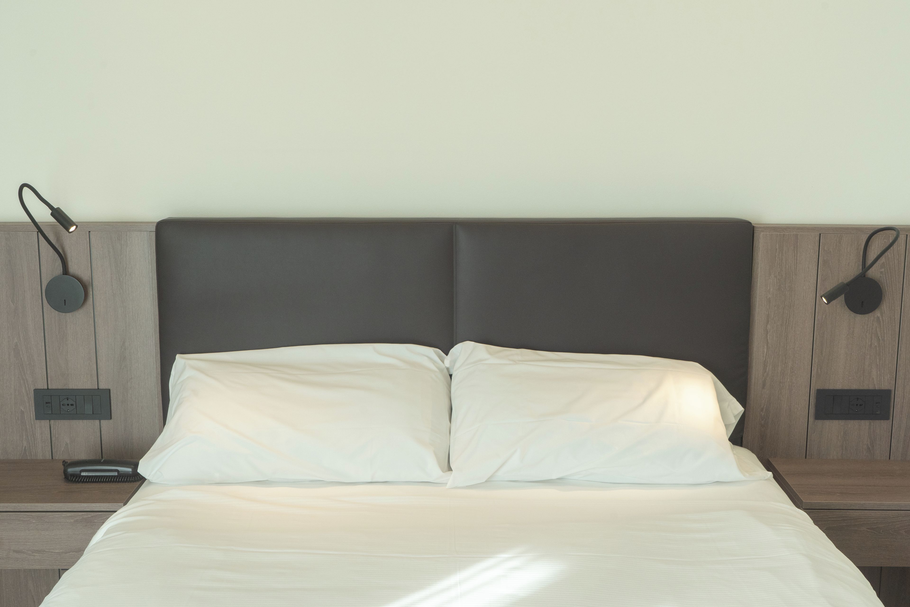 A bed with white bedding, a dark headboard, and two bedside lamps on wooden nightstands.
