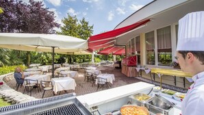 An outdoor dining area with tables and chairs, covered by umbrellas, and a grill station. - Hotel Terme Leonardo (Abano Terme)