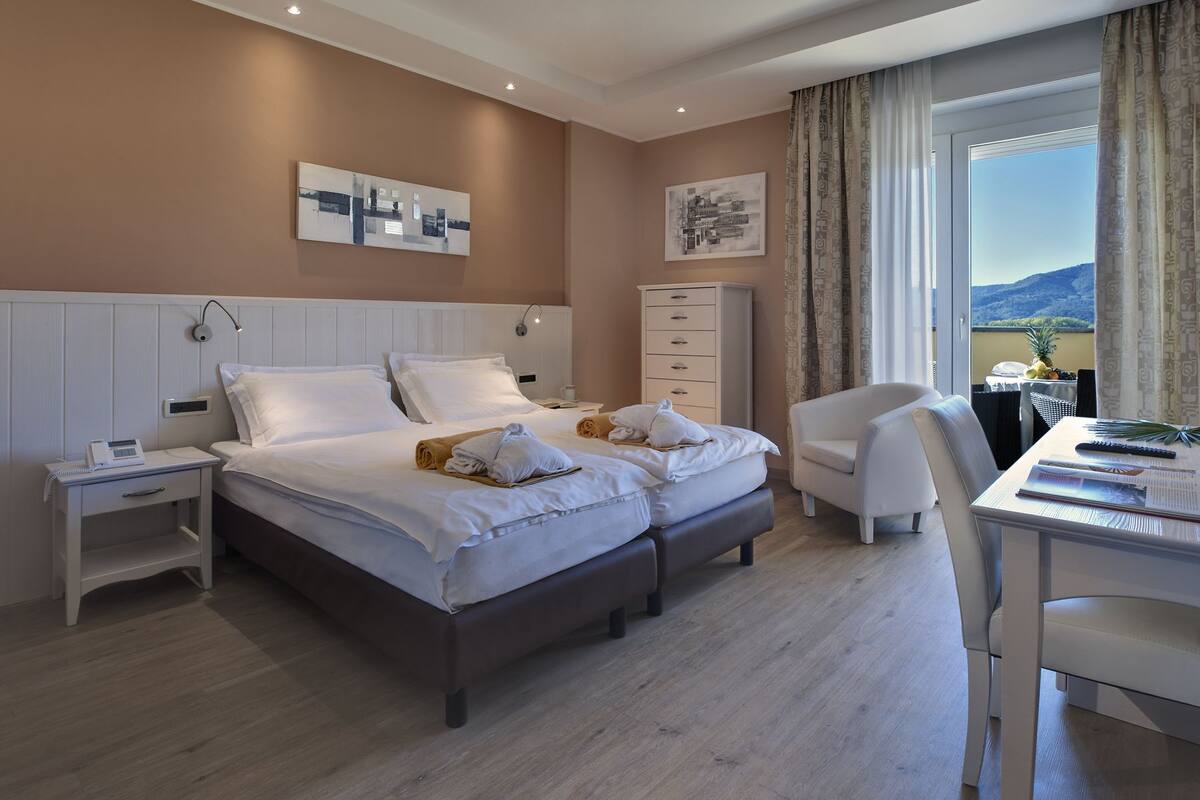 A hotel room with a double bed, a desk, a chair, a nightstand, a dresser, and two wall art pieces.