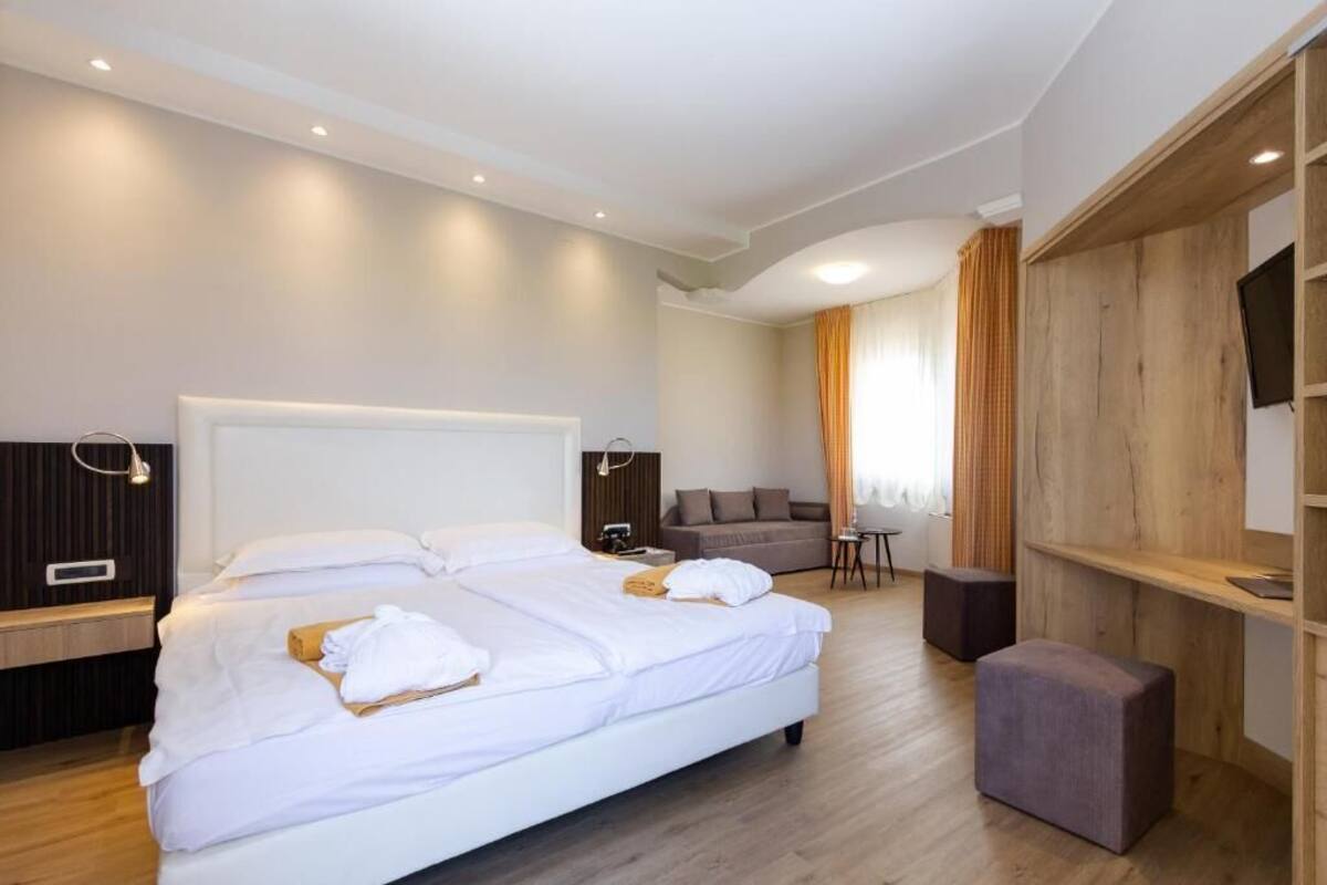 A modern hotel room with a large bed, a sofa, a TV, and a wooden accent wall.