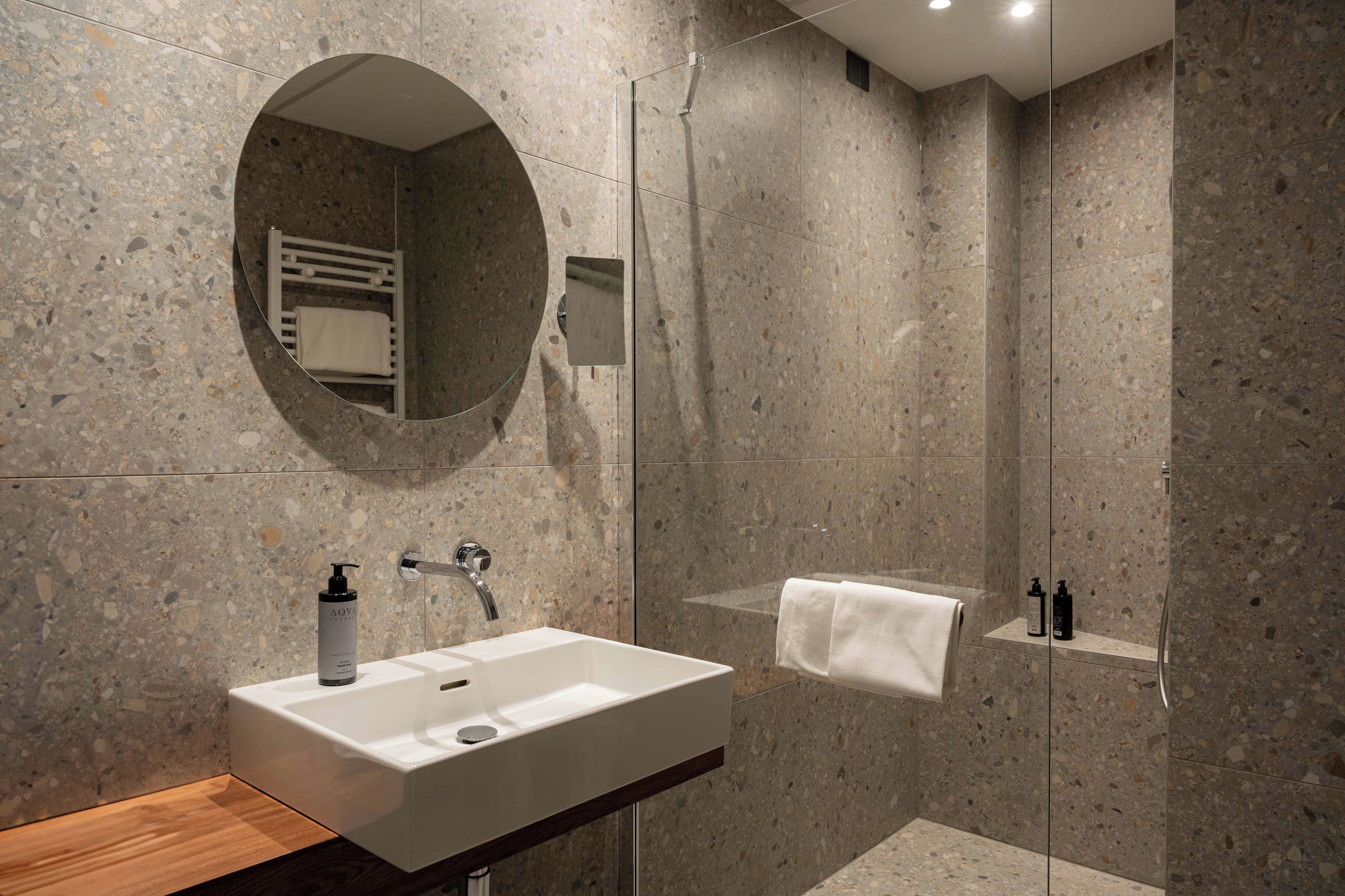A modern bathroom with a freestanding sink, a mirror, a towel rack, and a shower area.